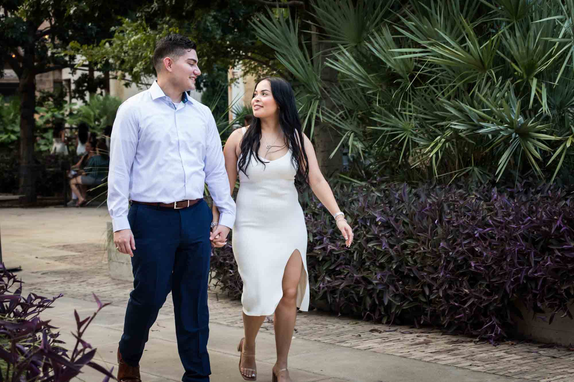 Couple walking hand-in-hand on sidewalk in front of palm tree during a Pearl engagement photo shoot