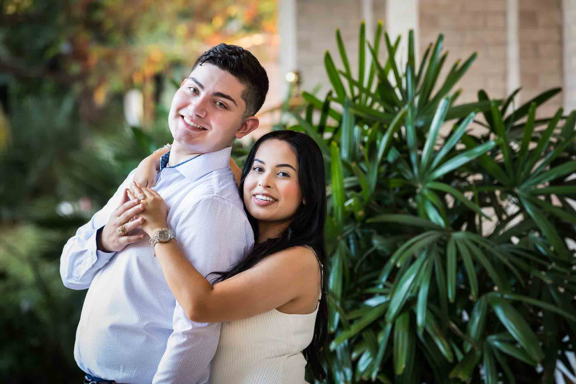 Couple hugging in front of palm leaves for an article on Pearl surprise proposal tips