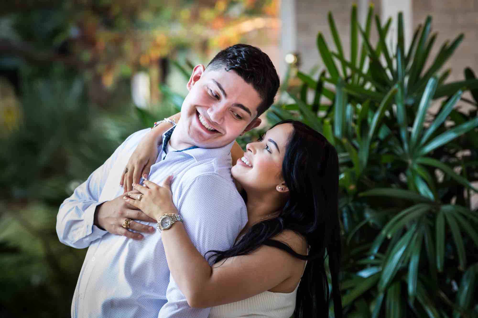 Couple hugging in front of palm leaves for an article on Pearl surprise proposal tips