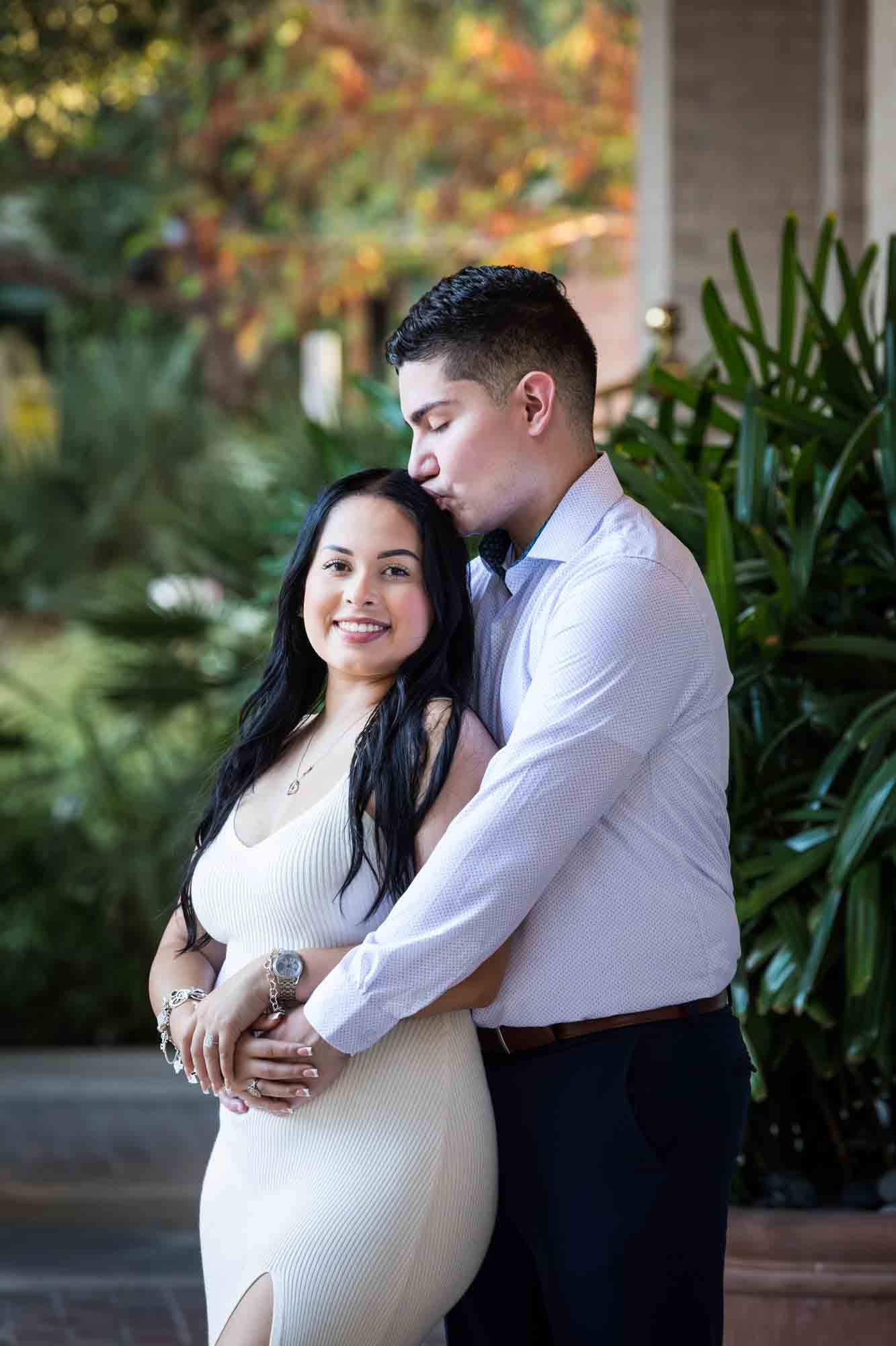 Man kissing woman on head in front of palm leaves for an article on Pearl surprise proposal tips