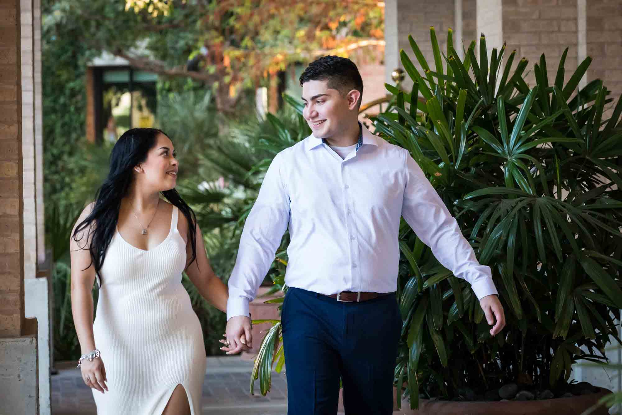 Couple walking hand-in-hand in front of palm leaves for an article on Pearl surprise proposal tips