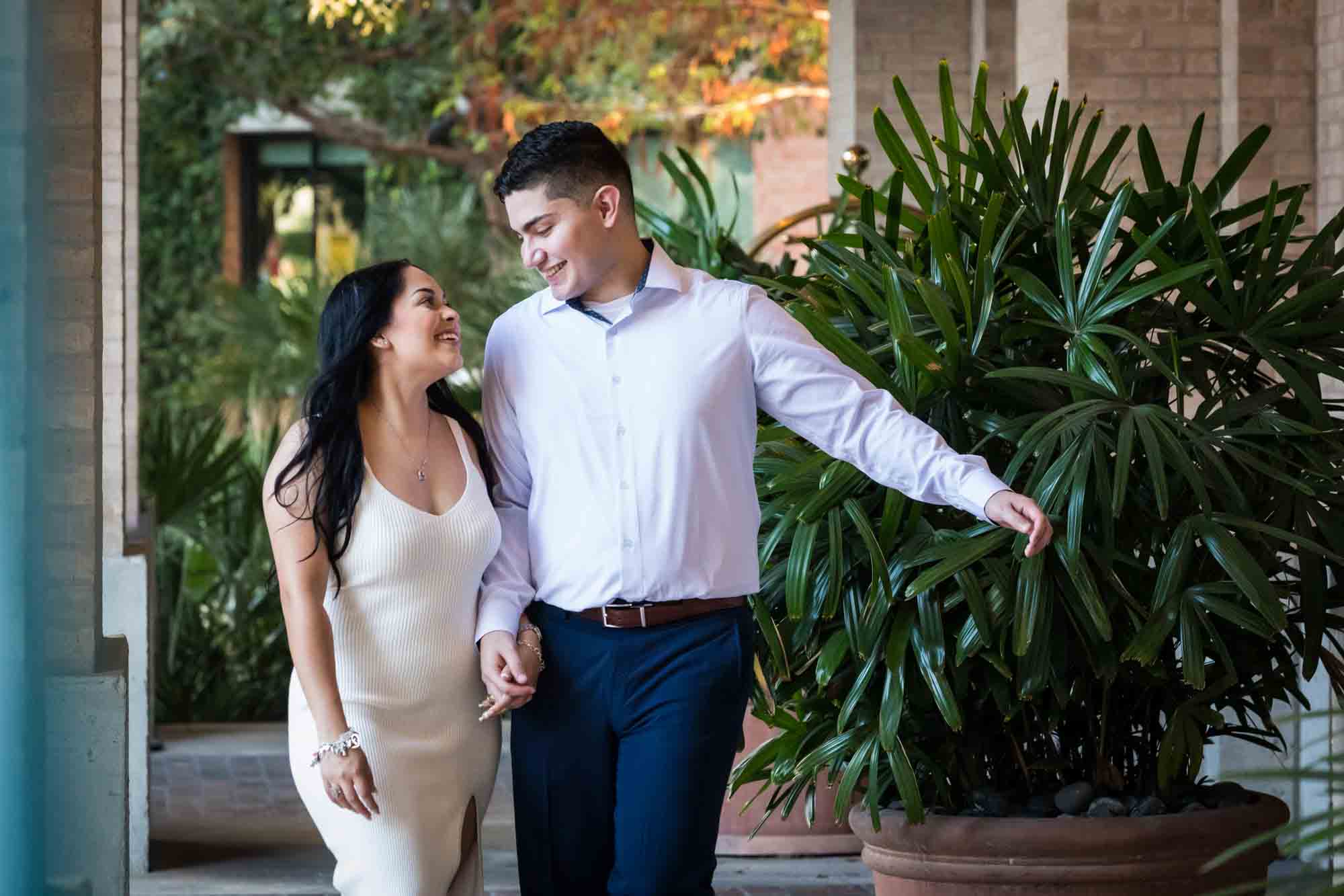 Couple walking hand-in-hand in front of palm leaves for an article on Pearl surprise proposal tips