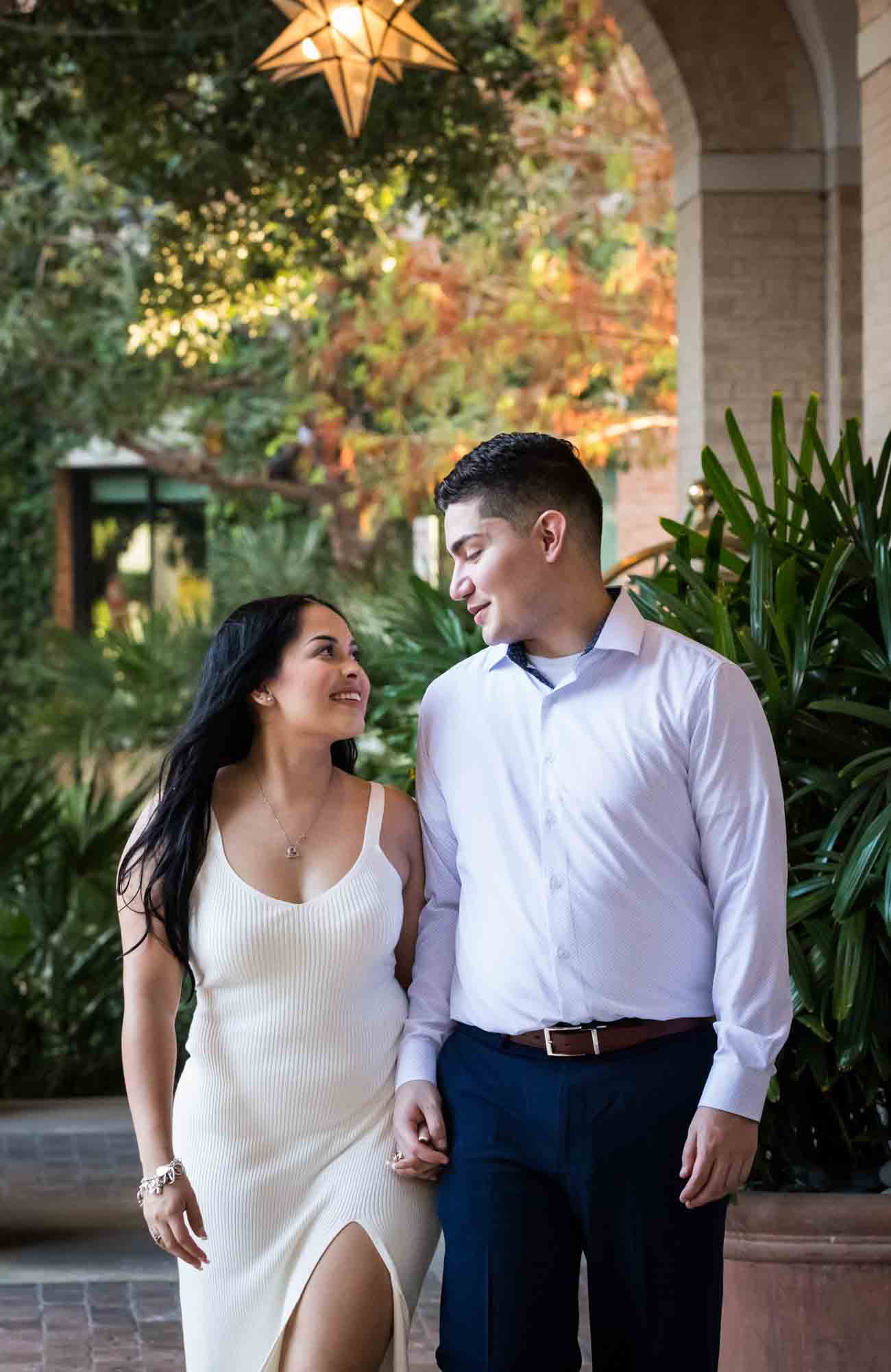 Couple walking hand-in-hand in front of palm leaves for an article on Pearl surprise proposal tips