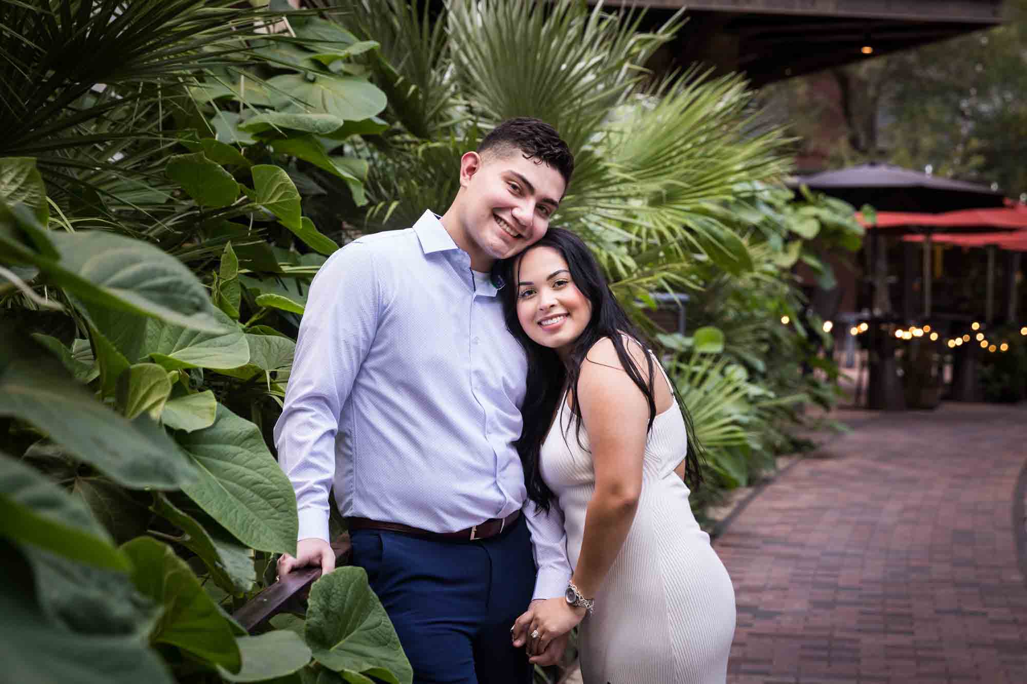 Couple hugging in front of large green leaves for an article on Pearl surprise proposal tips