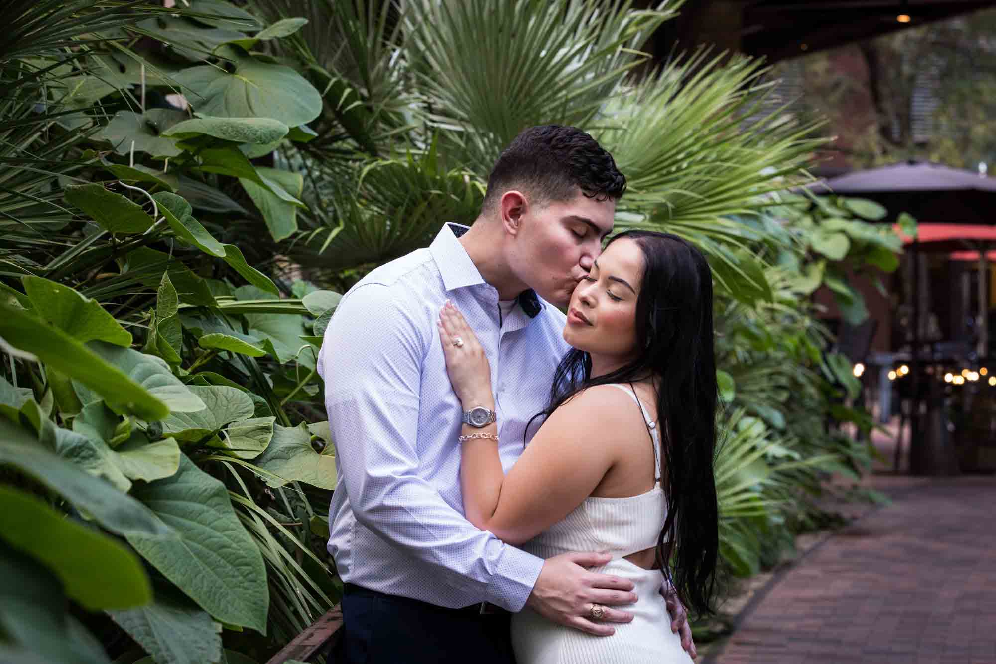 Man kissing woman in front of large green leaves for an article on Pearl surprise proposal tips