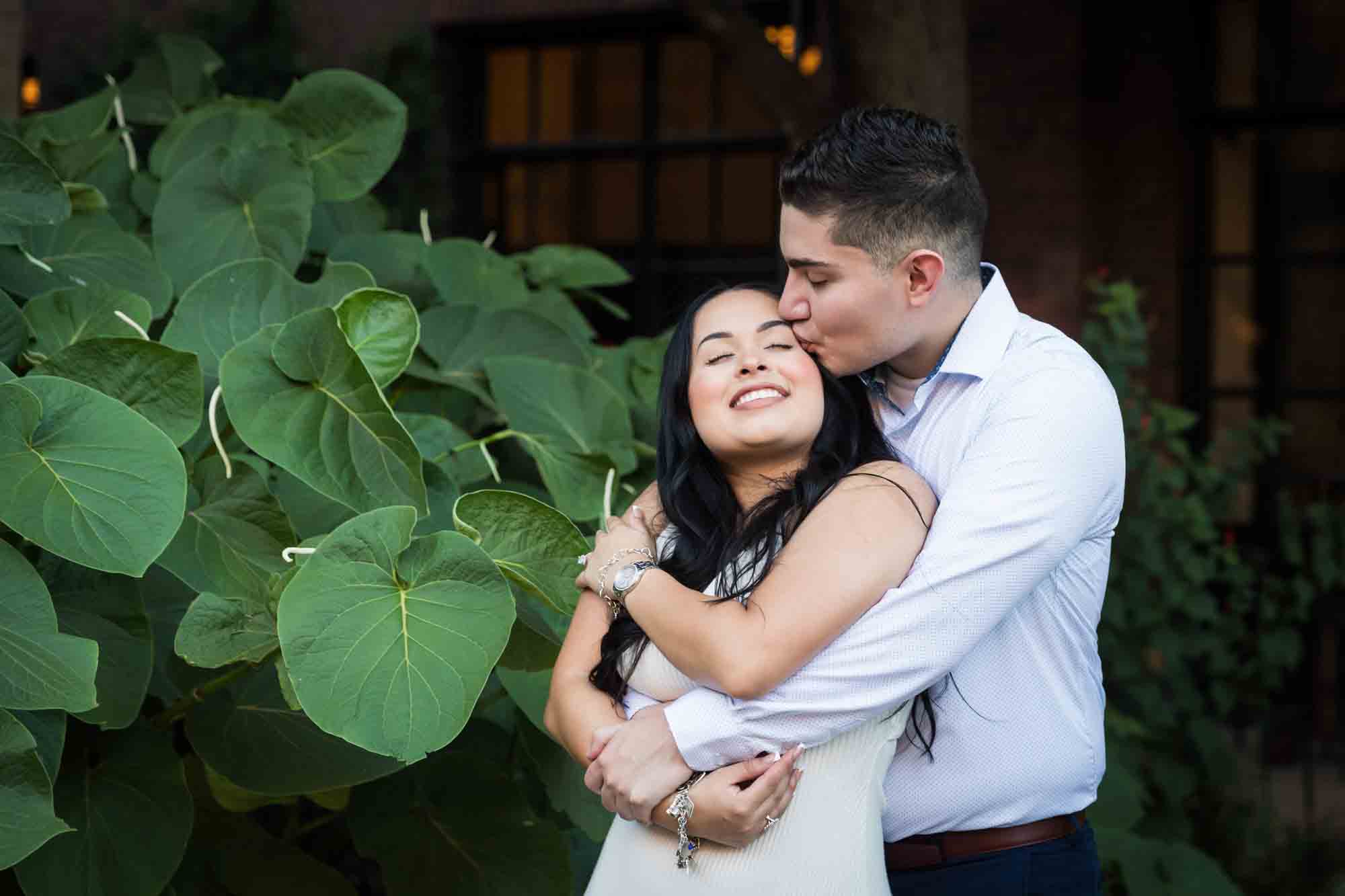 Couple hugging in front of large green leaves for an article on Pearl surprise proposal tips