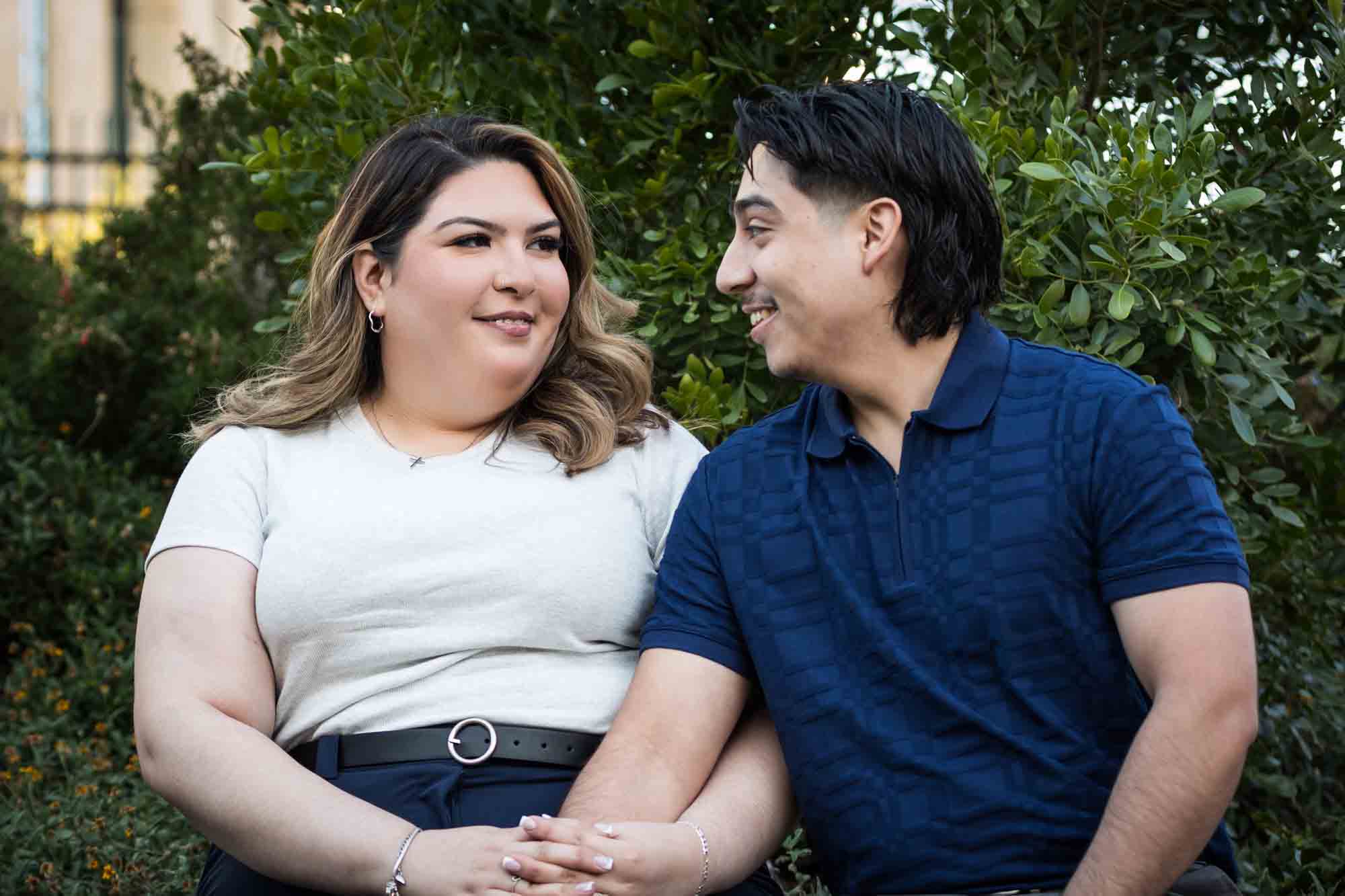 Couple sitting on bench in front of green bushes during a downtown San Antonio photo shoot