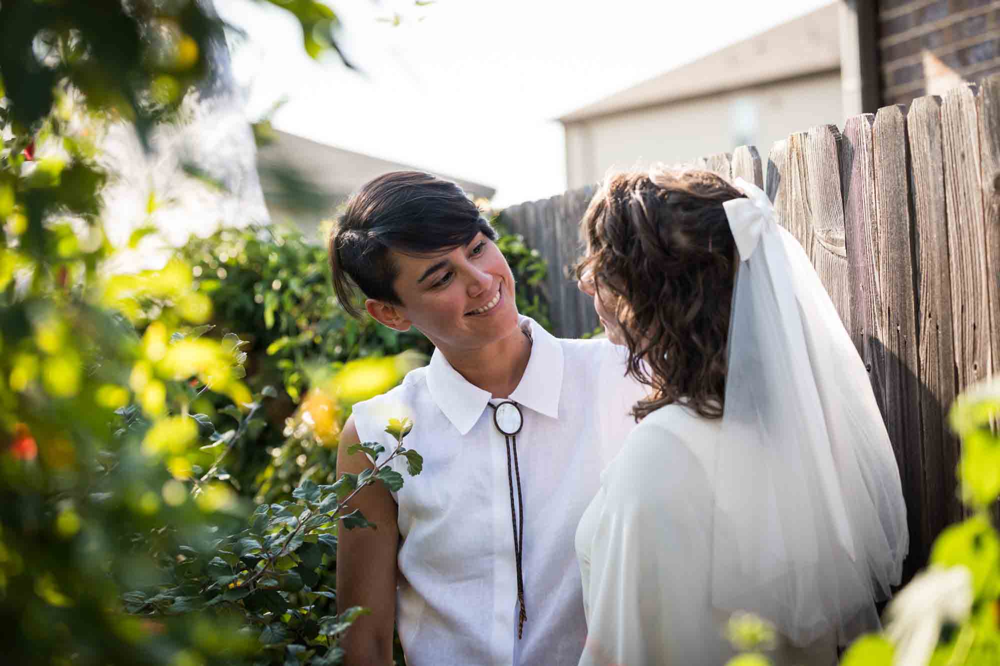 Two brides wearing white and hugging surrounded by plants at a Boerne backyard wedding