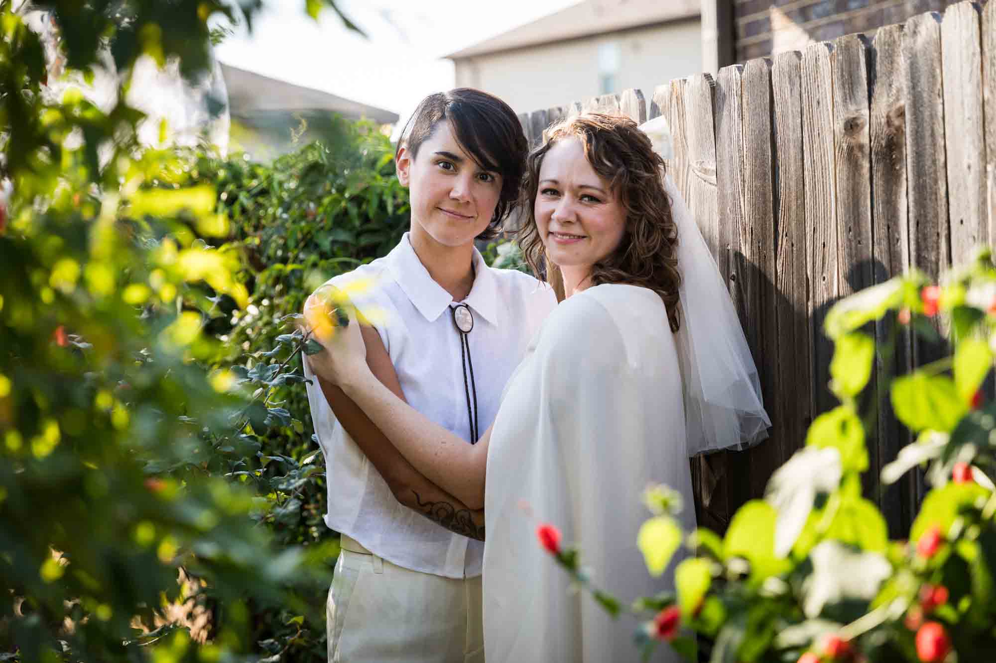 Two brides wearing white and hugging surrounded by plants at a Boerne backyard wedding