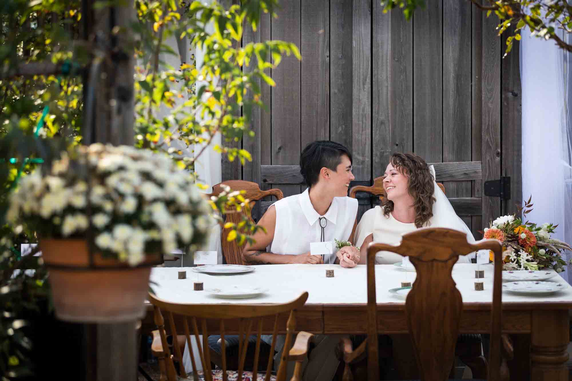 Two brides seated outside at a table surrounded by plants at a Boerne backyard wedding