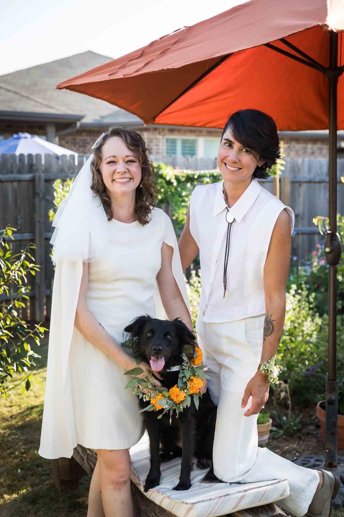 Two brides wearing white with black dog wearing flower collar at a Boerne backyard wedding