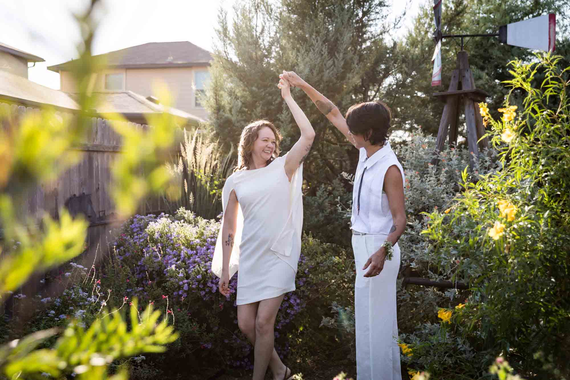 Two brides wearing white and dancing surrounded by plants at a Boerne backyard wedding