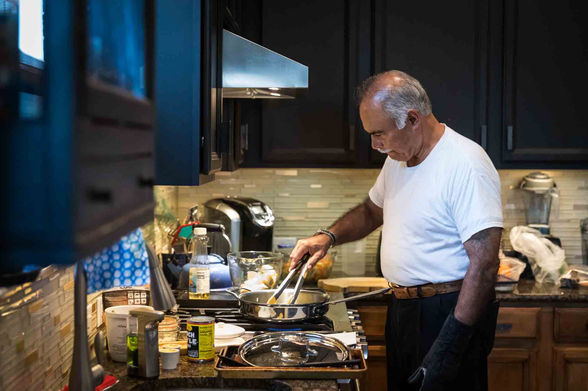 Older man wearing white t-shirt cooking over a stove in a kitchen