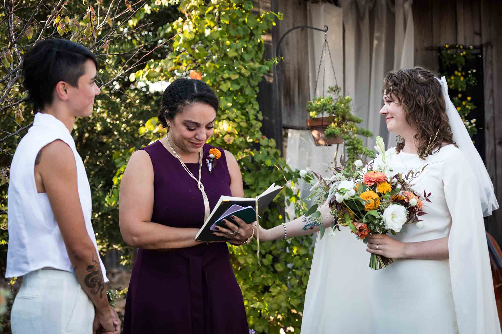 Female officiant in maroon dress reading in front of two brides at a Boerne backyard wedding