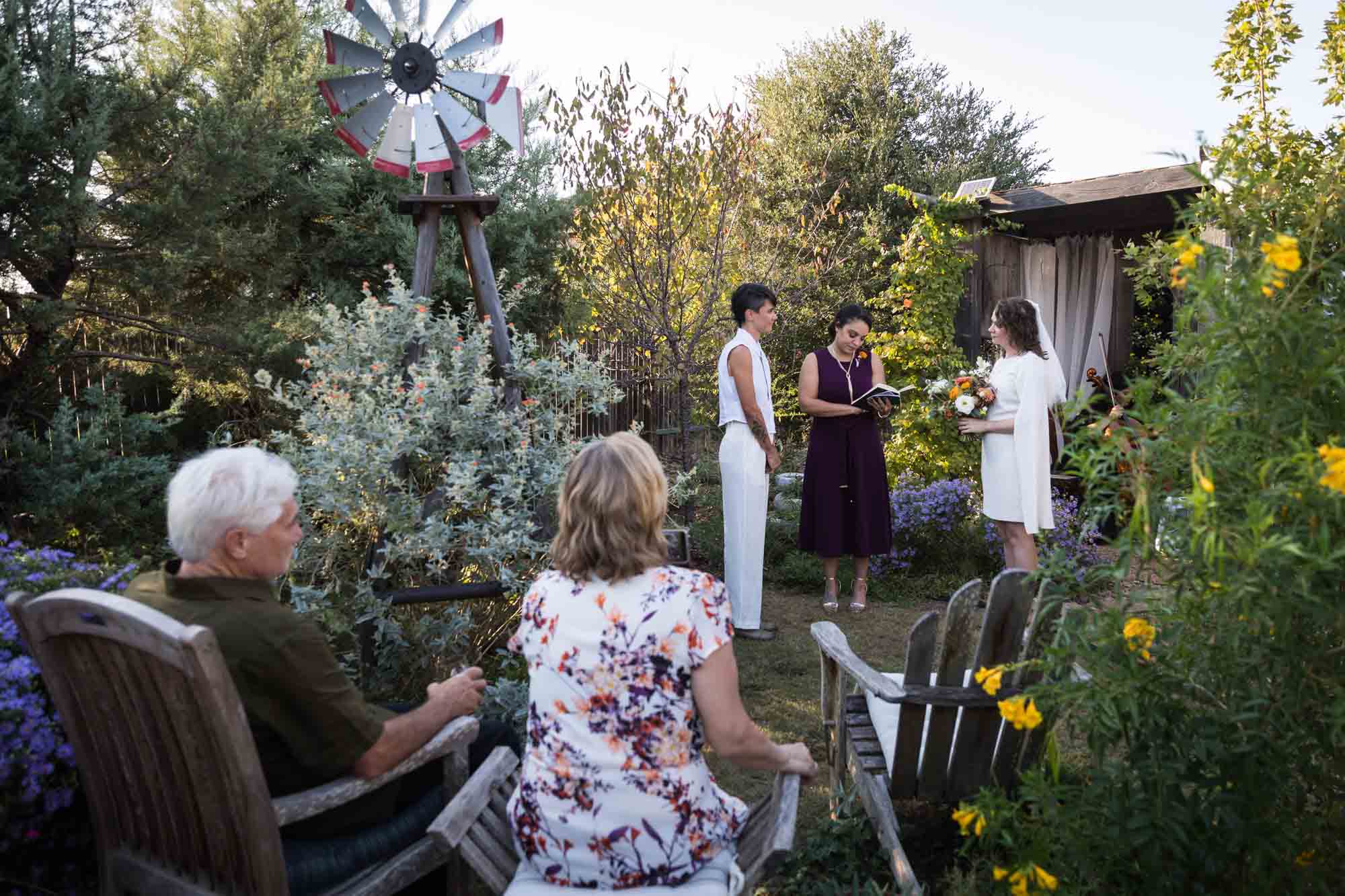 Two brides standing with officiant in front of guests at a Boerne backyard wedding