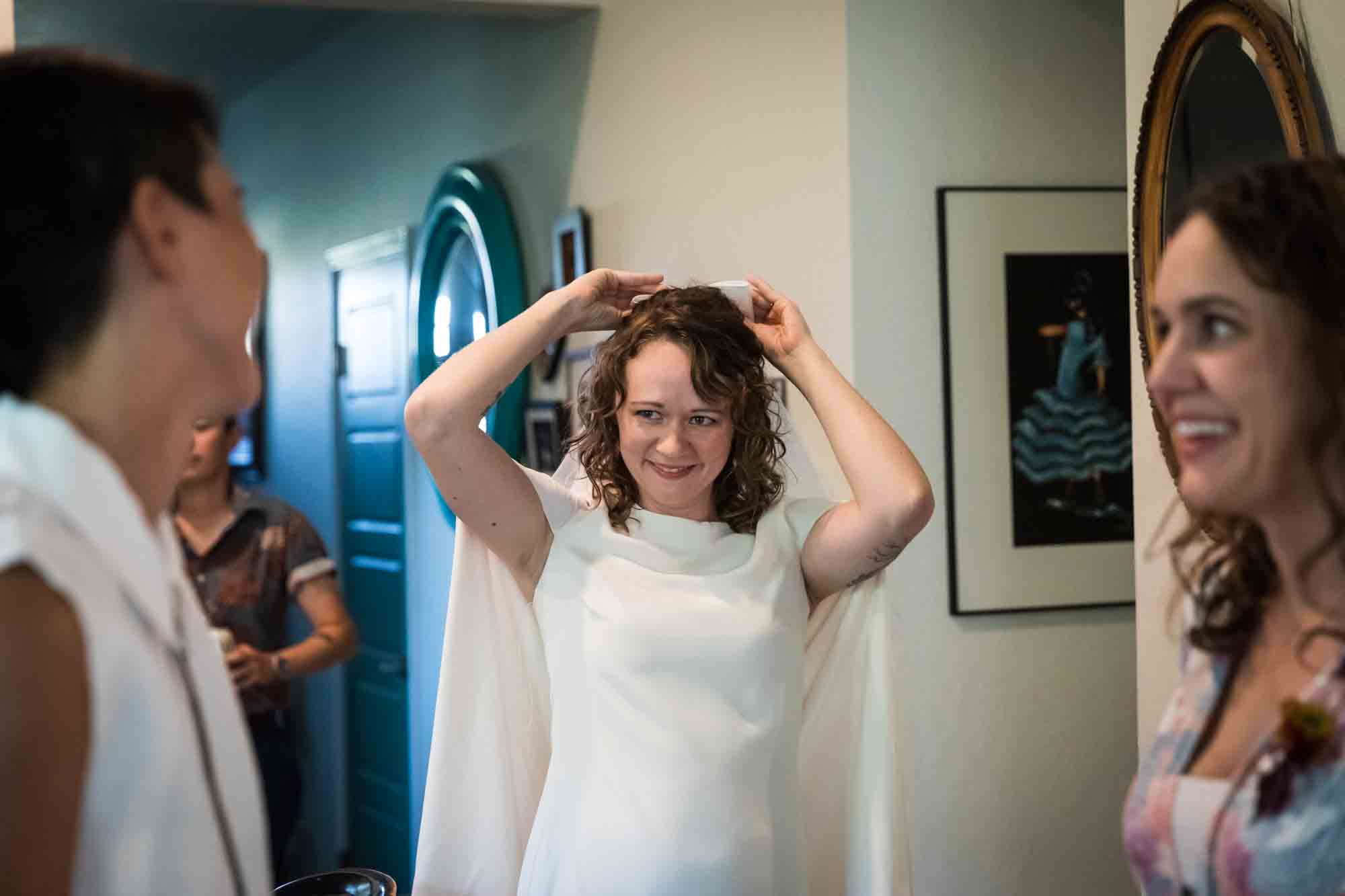 Bride adjusting veil in home in front of two other women