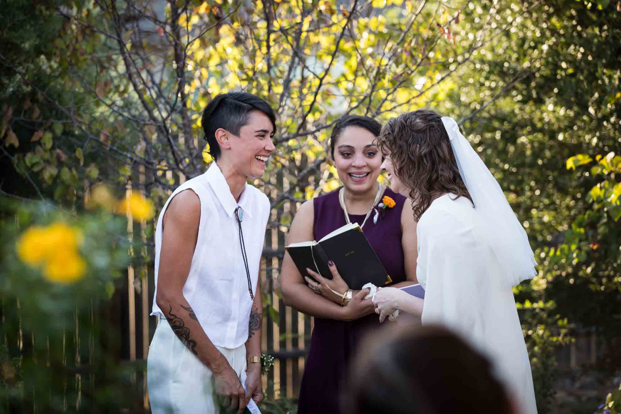 Two brides laughing in front of officiant and guests at a Boerne backyard wedding