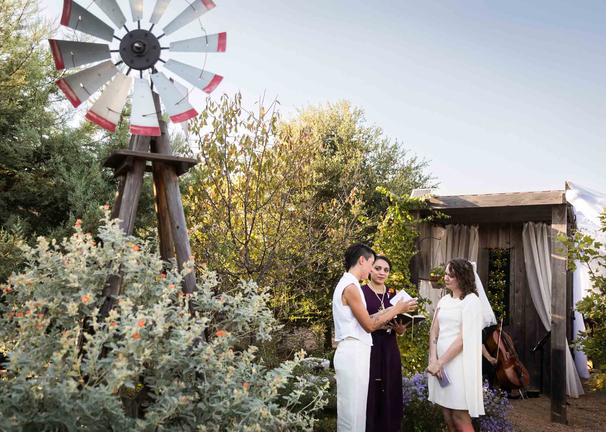 Two brides exchanging vows in front of officiant and windmill at a Boerne backyard wedding