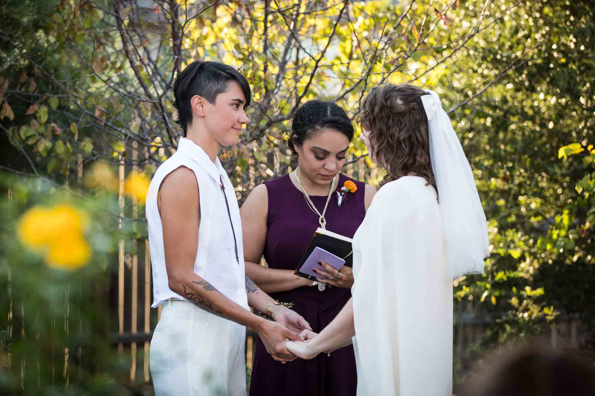 Two brides holding hands in front of officiant at a Boerne backyard wedding