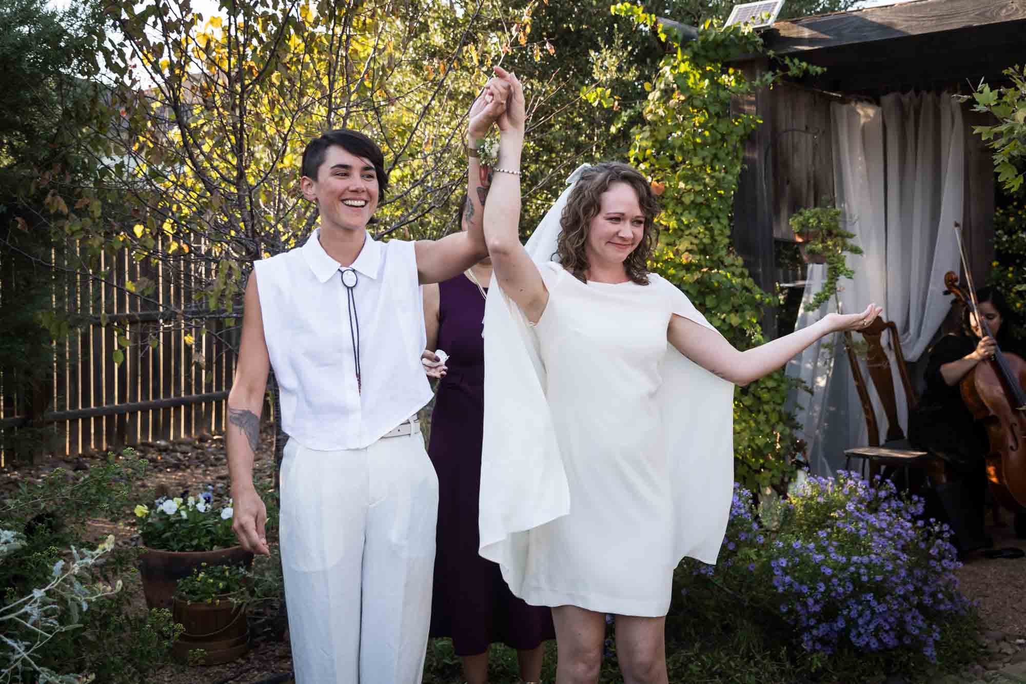 Two brides holding hands in the air at a Boerne backyard wedding