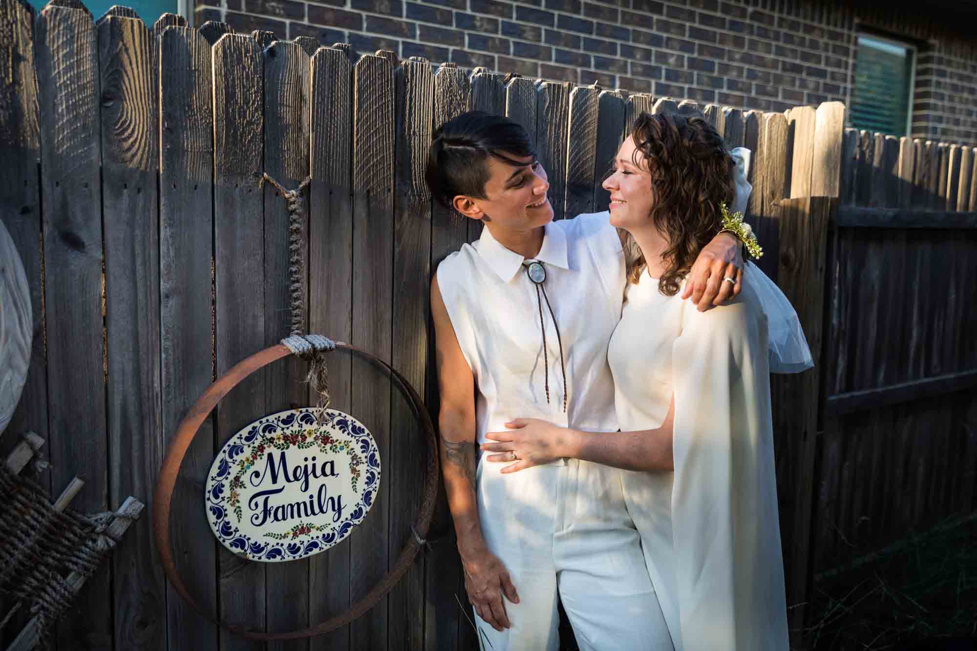 Two brides hugging against wooden fence