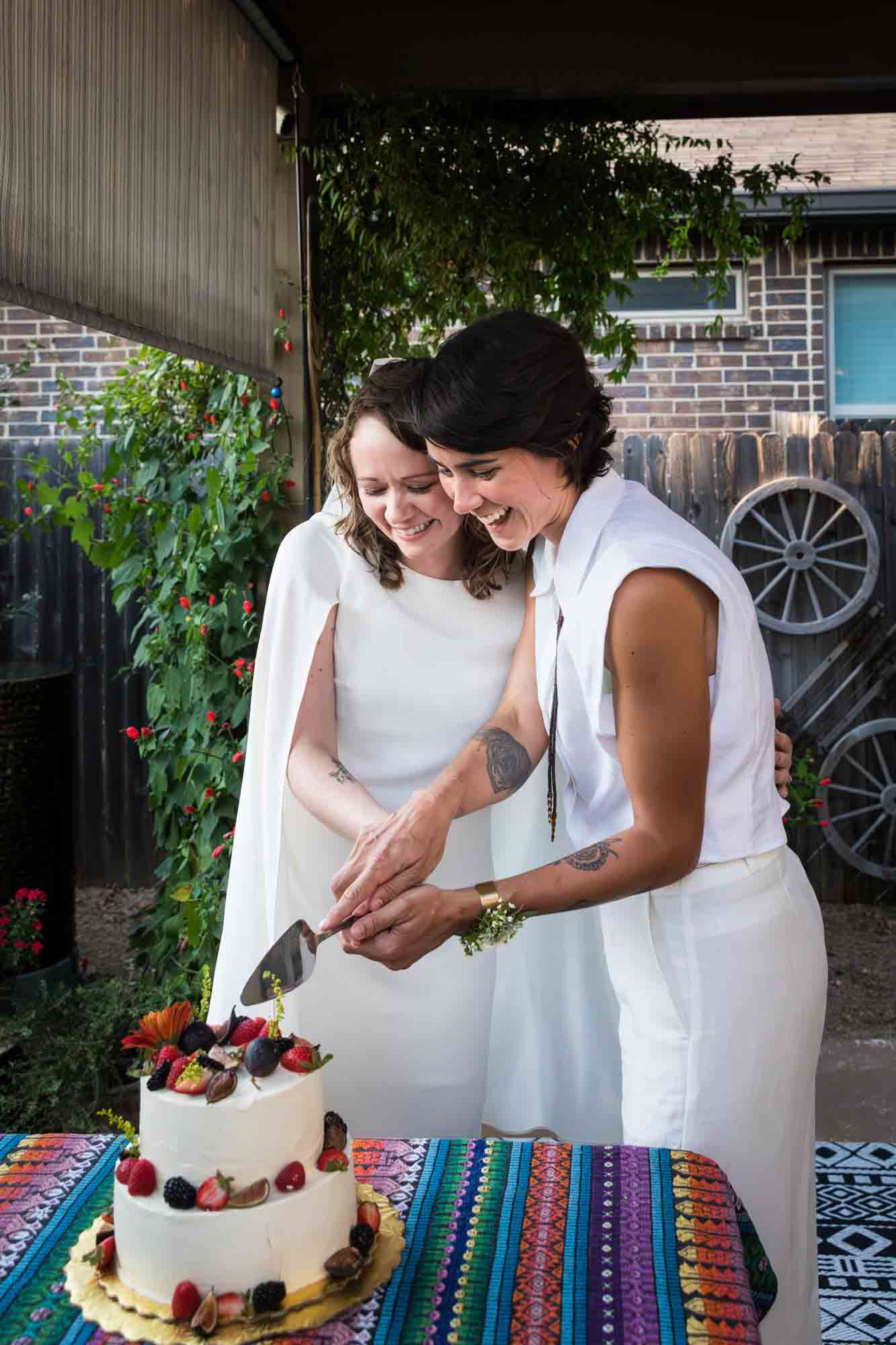 Two brides cutting a wedding cake with fruit on top at a Boerne backyard wedding