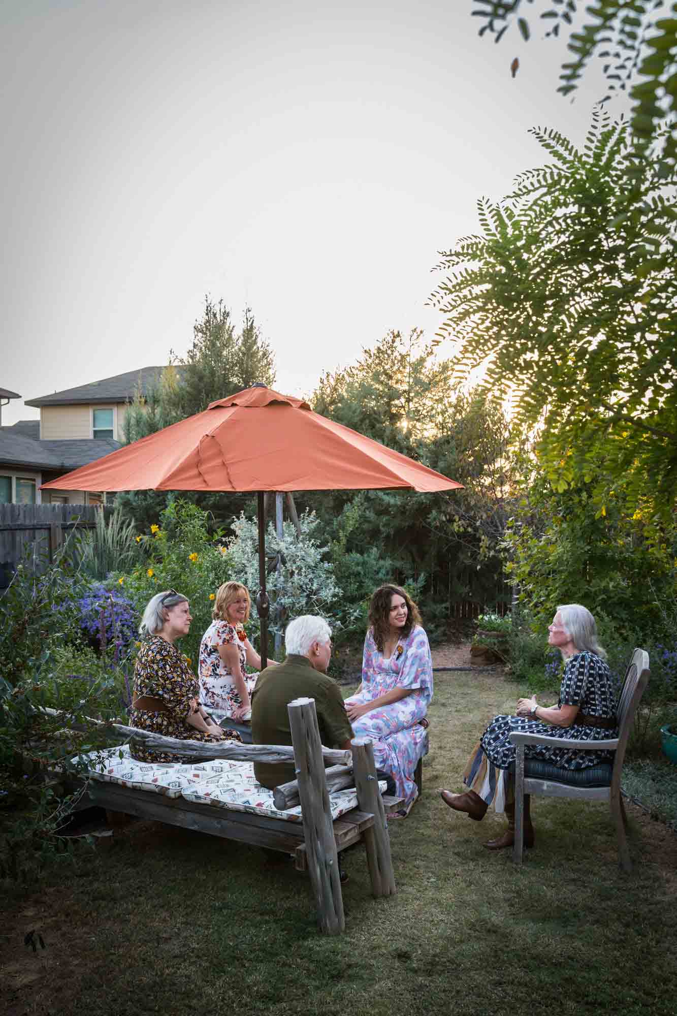 Group of guests seated outside under a red umbrella at a Boerne backyard wedding