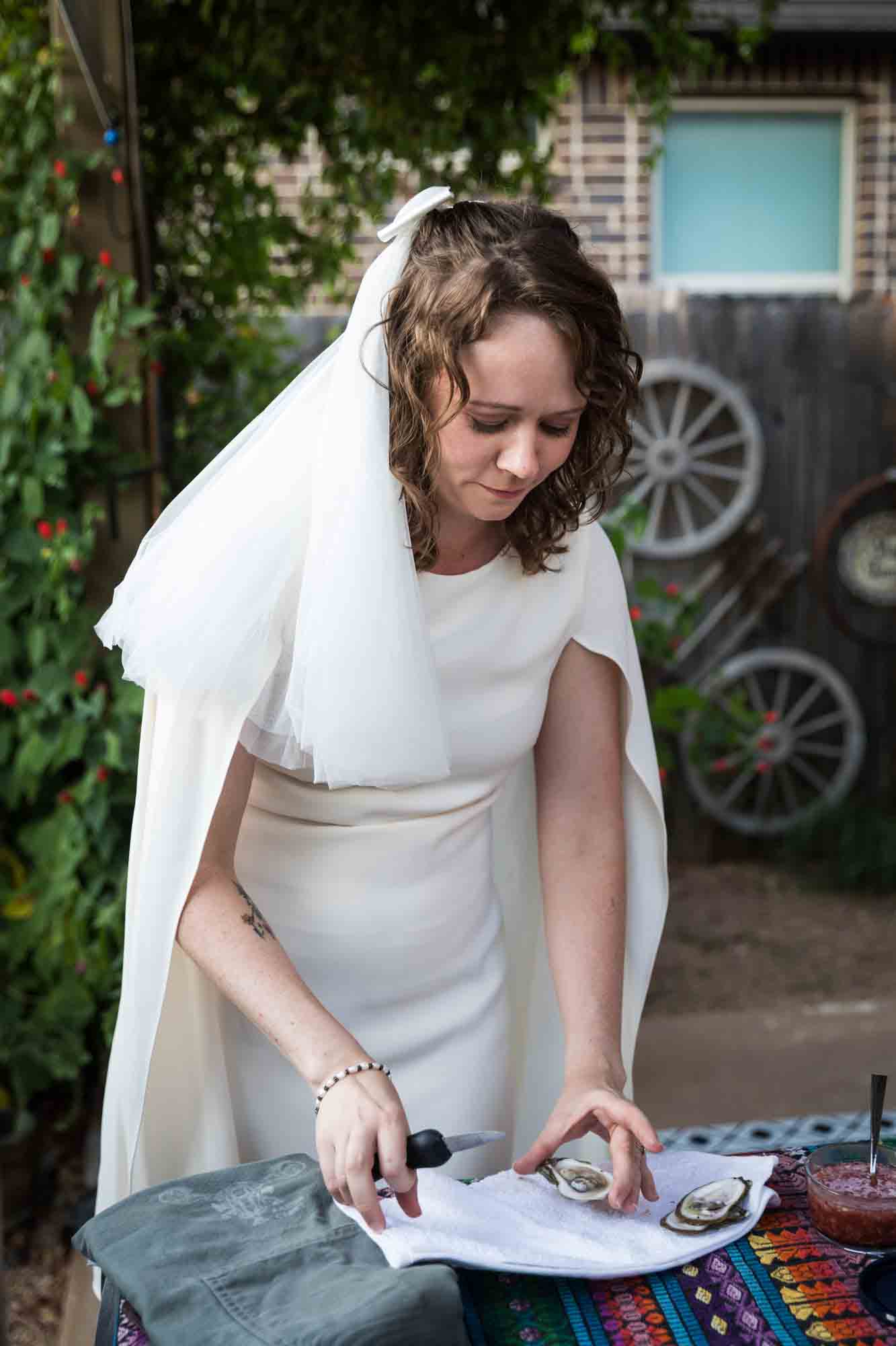 Bride wearing white dress and veil while shucking oysters over table