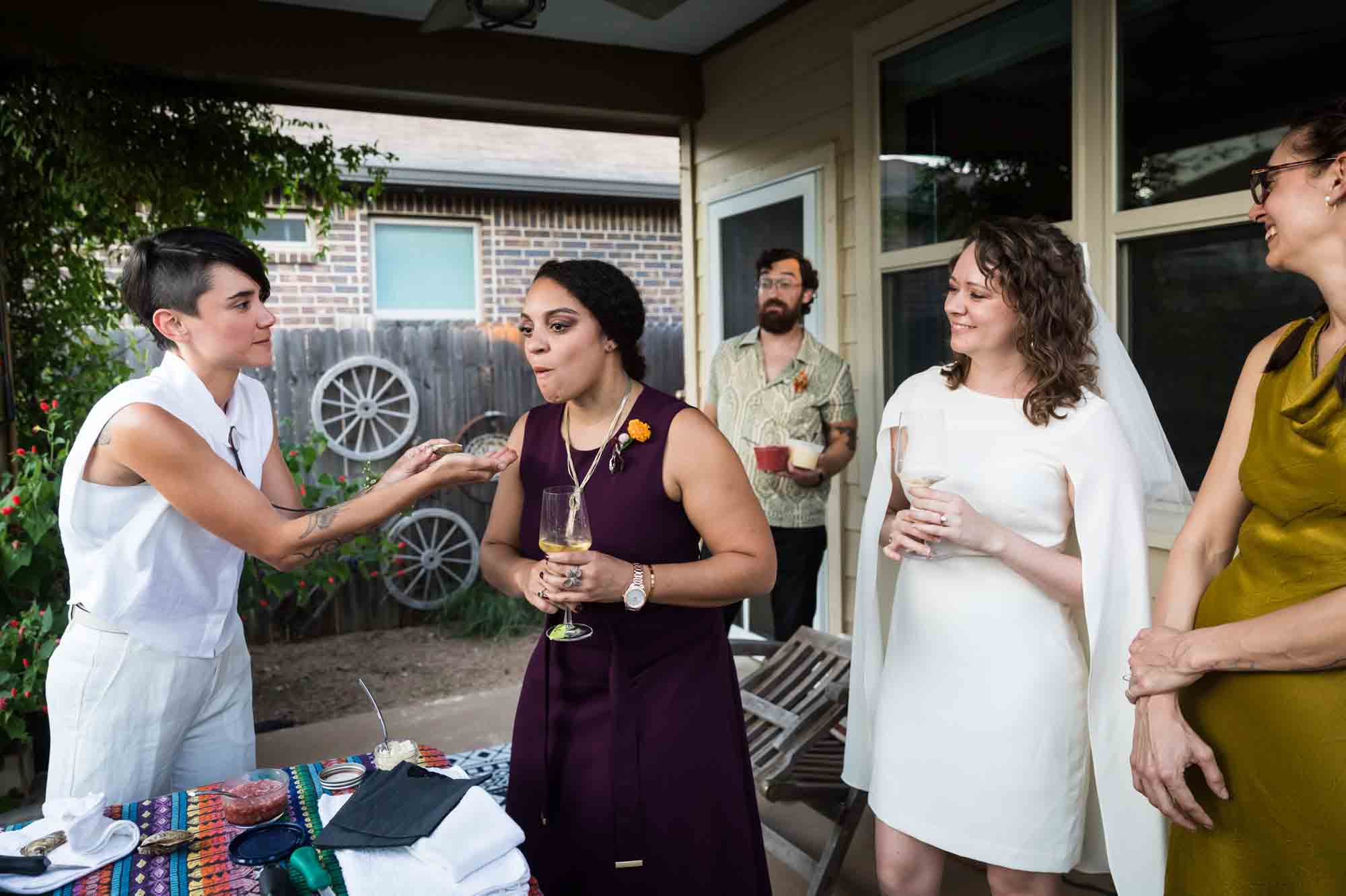 Bride feeding oyster to woman in maroon dress with guests watching