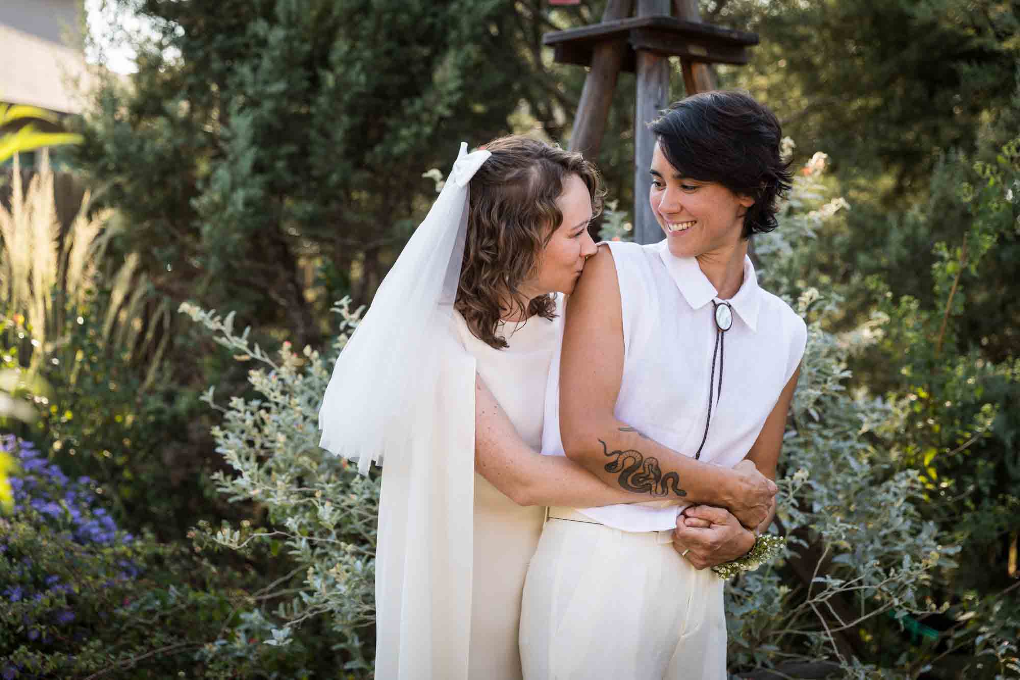 Two brides wearing white and one bride kissing the other on the shoulder at a Boerne backyard wedding