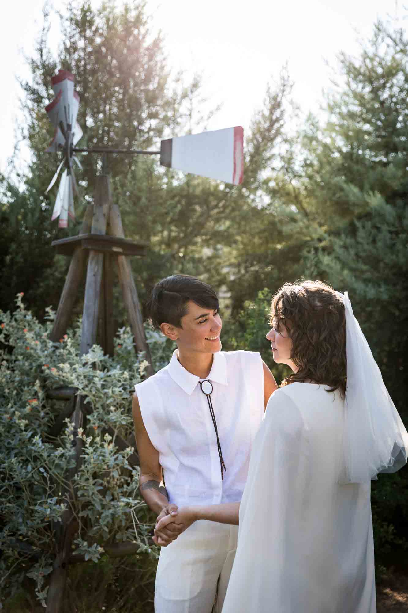 Two brides wearing white and hugging surrounded by plants at a Boerne backyard wedding