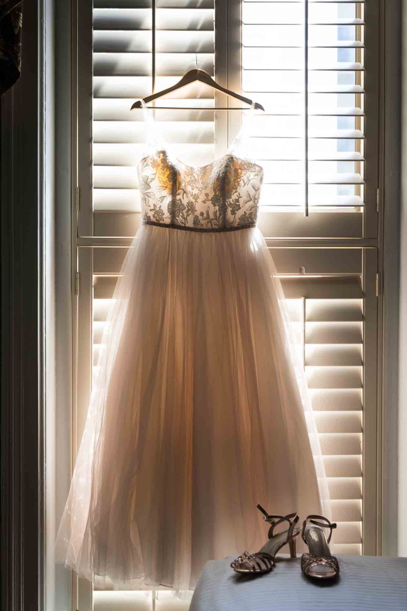 Off-white wedding dress hanging in front of a window at the Menger Hotel