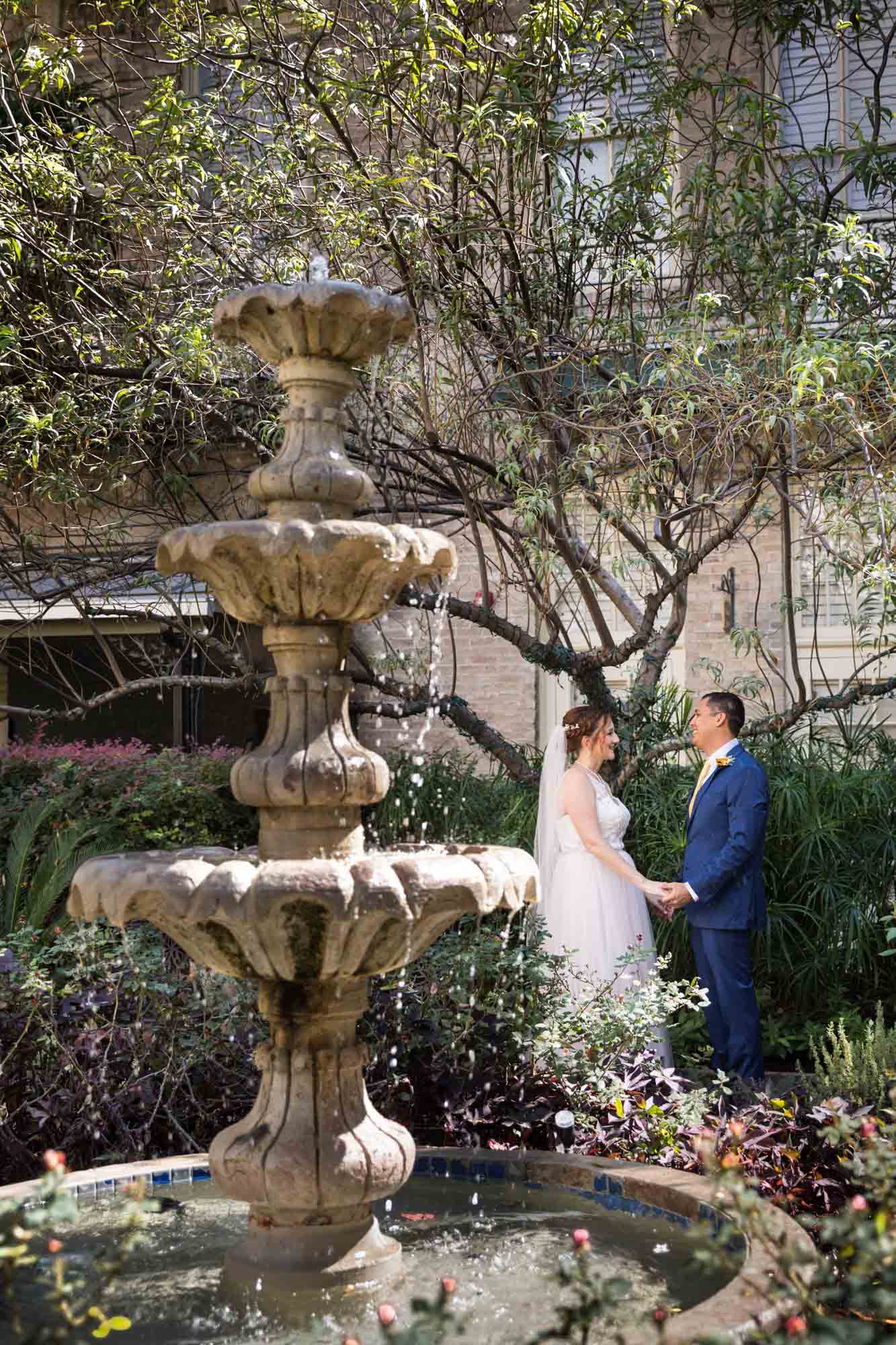 Bride and groom dancing in plant-filled courtyard behind stone fountain at the Menger Hotel