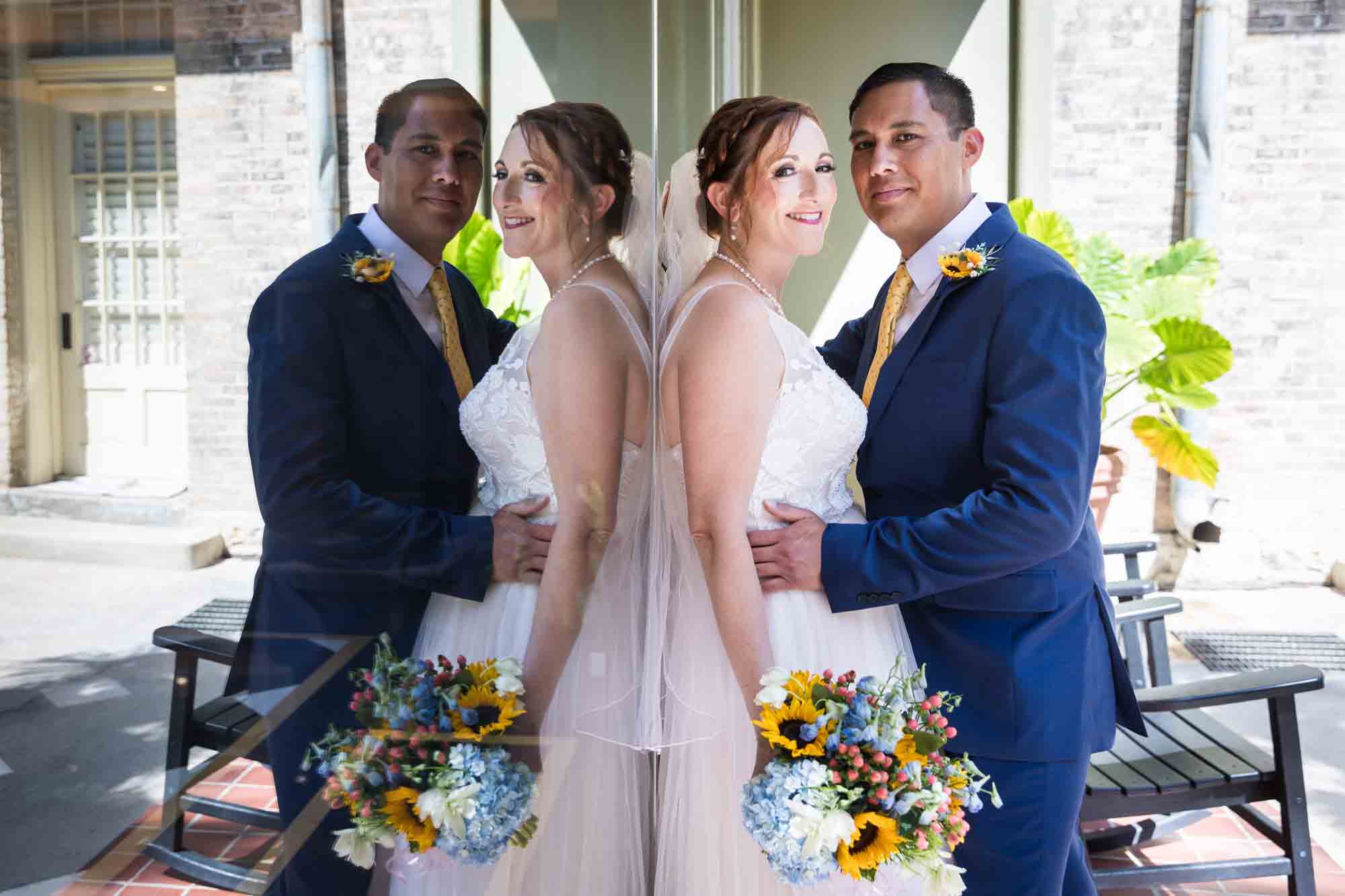 Bride and groom standing against reflective window at the Menger Hotel