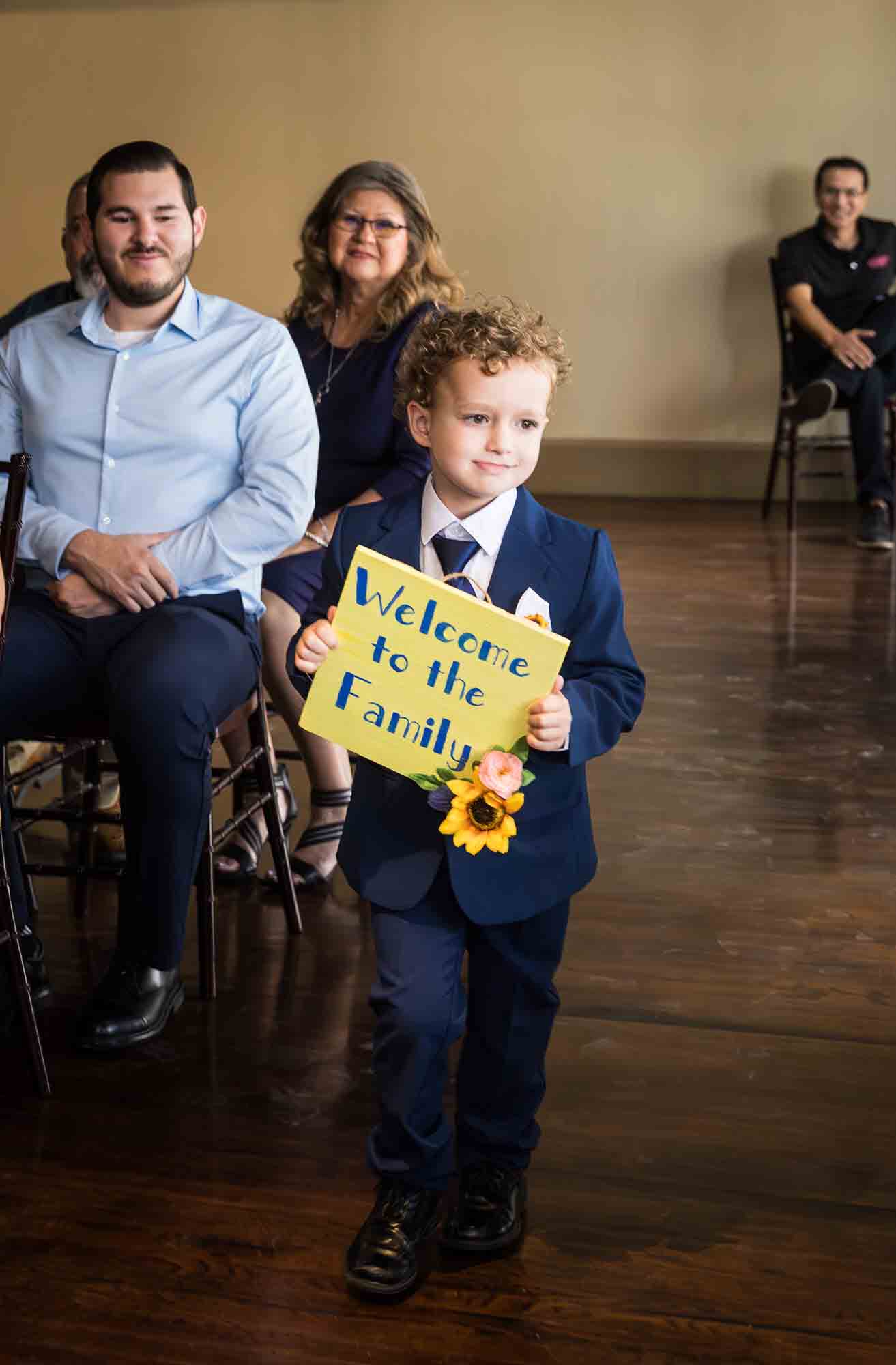 Pat O’Brien wedding photos of a little boy holding yellow sign down aisle during ceremony