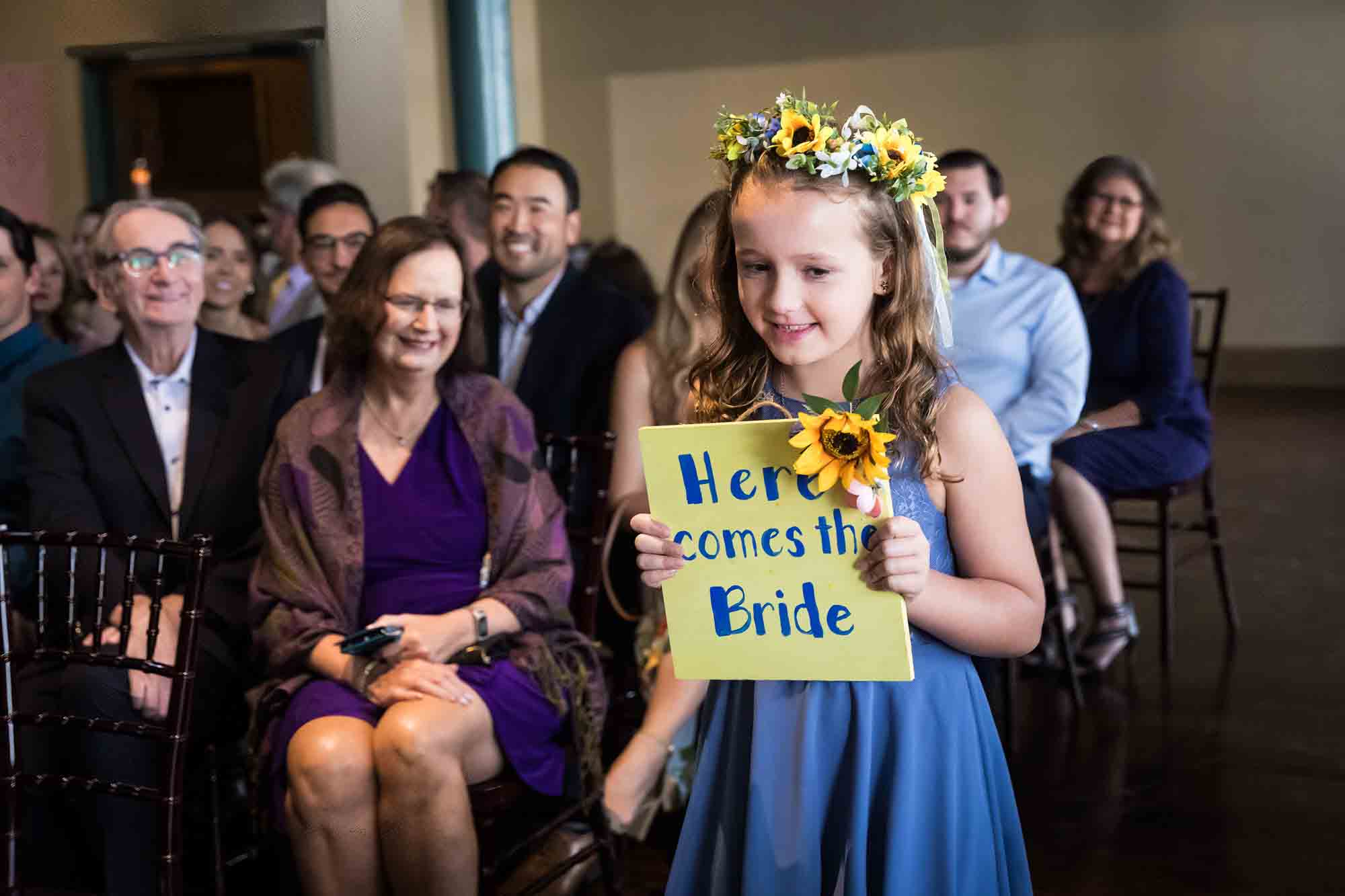 Pat O’Brien wedding photos of a flower girl holding yellow sign down aisle during ceremony