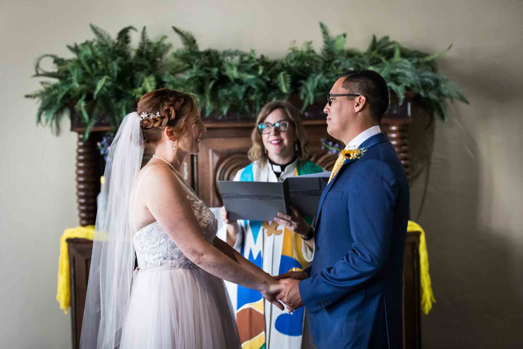 Pat O’Brien wedding photos of bride and groom holding hands in front of pastor during ceremony