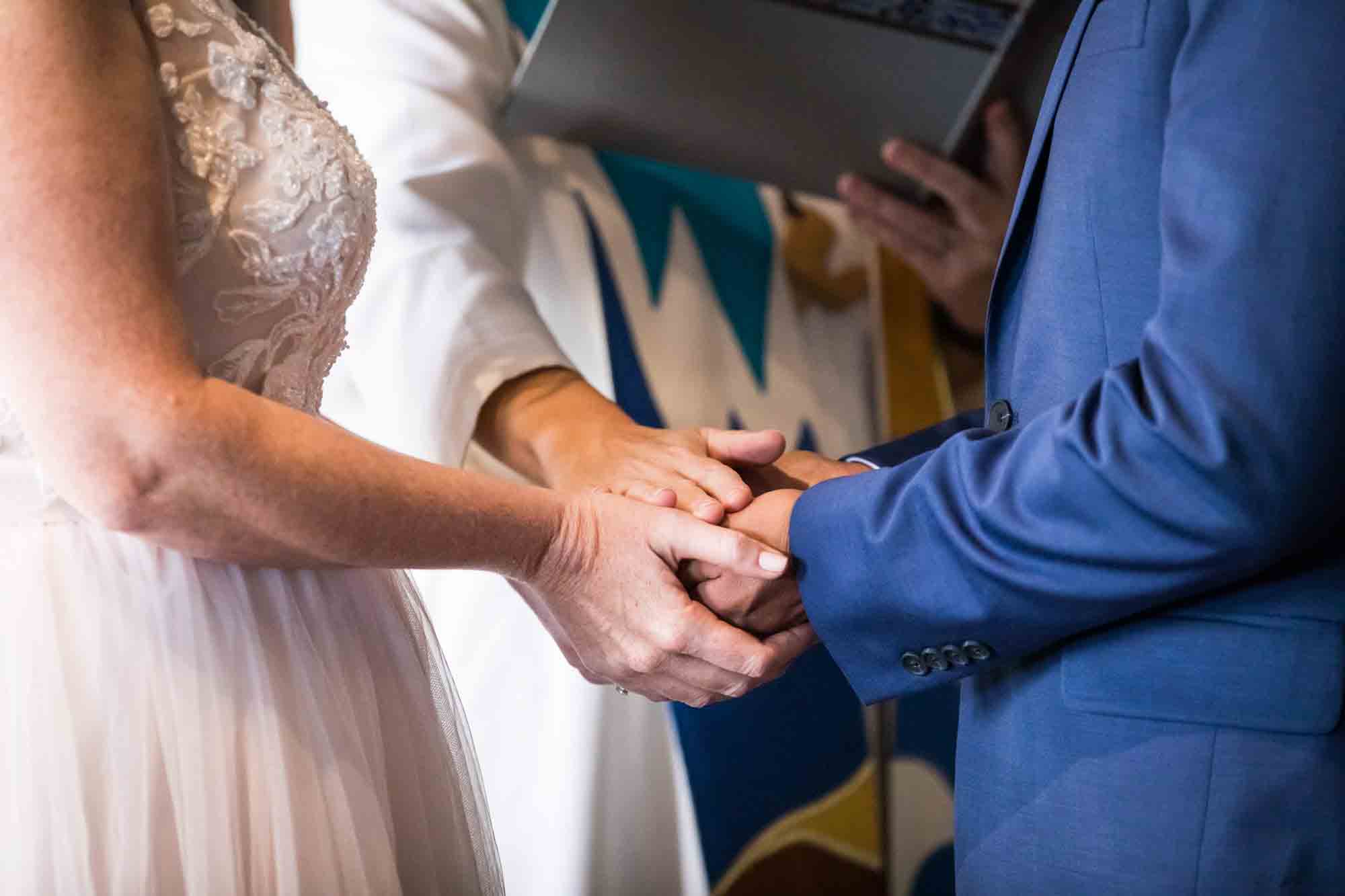 Close up of bride and groom holding hands with pastor's hand on top during ceremony blessing