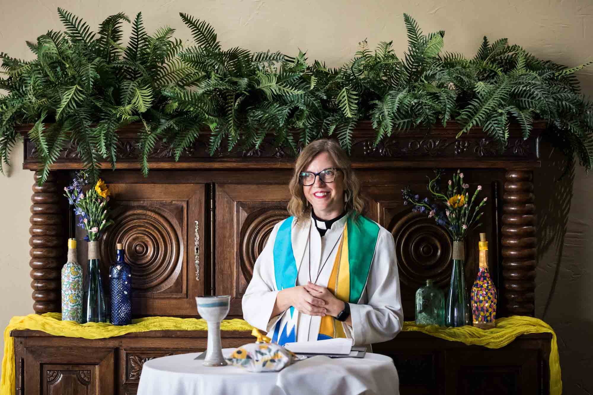 Pat O’Brien wedding photos of pastor wearing colorful collar behind table with communion cup