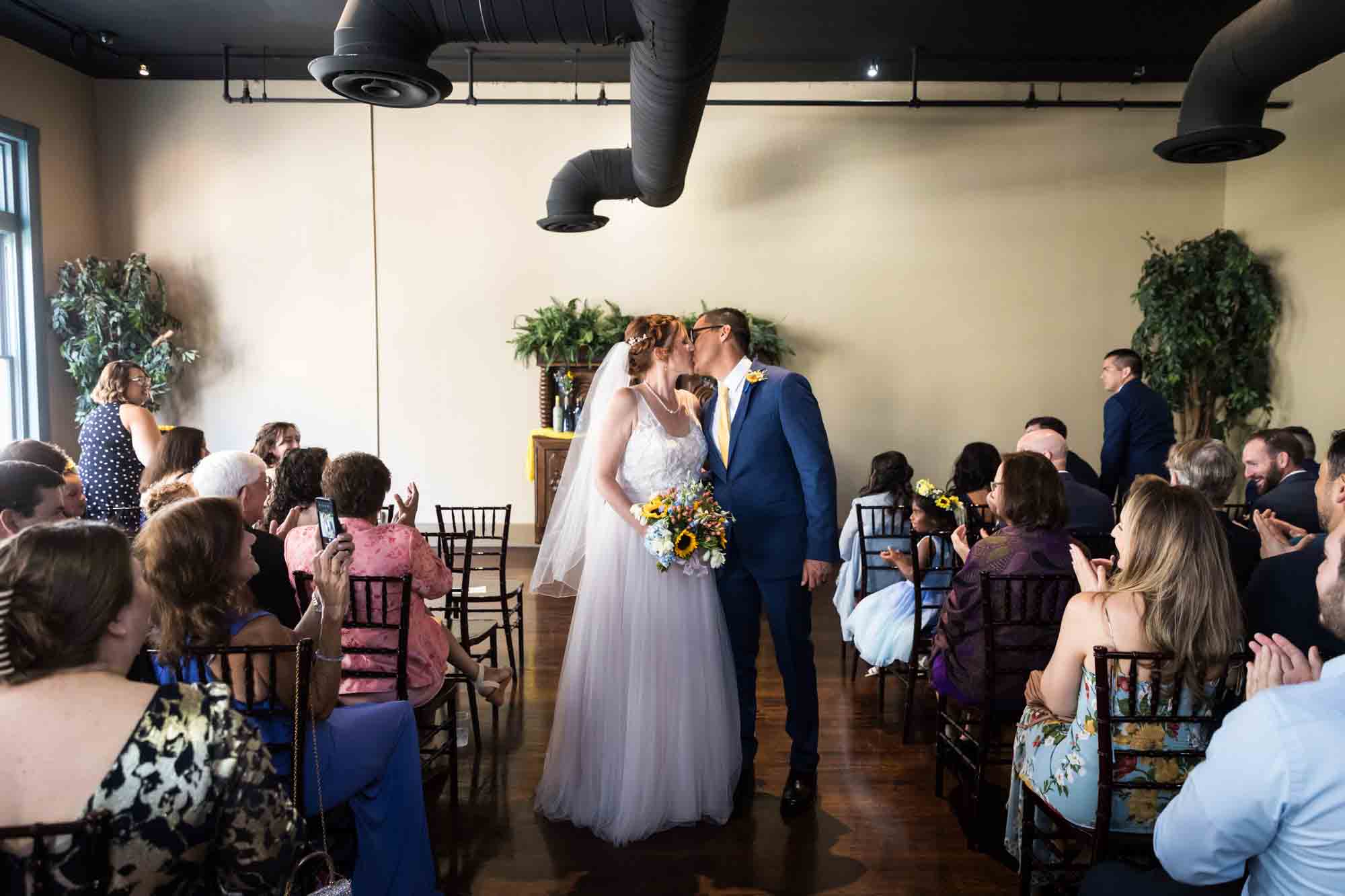 Pat O’Brien wedding photos of bride and groom kissing in aisle in front of guests