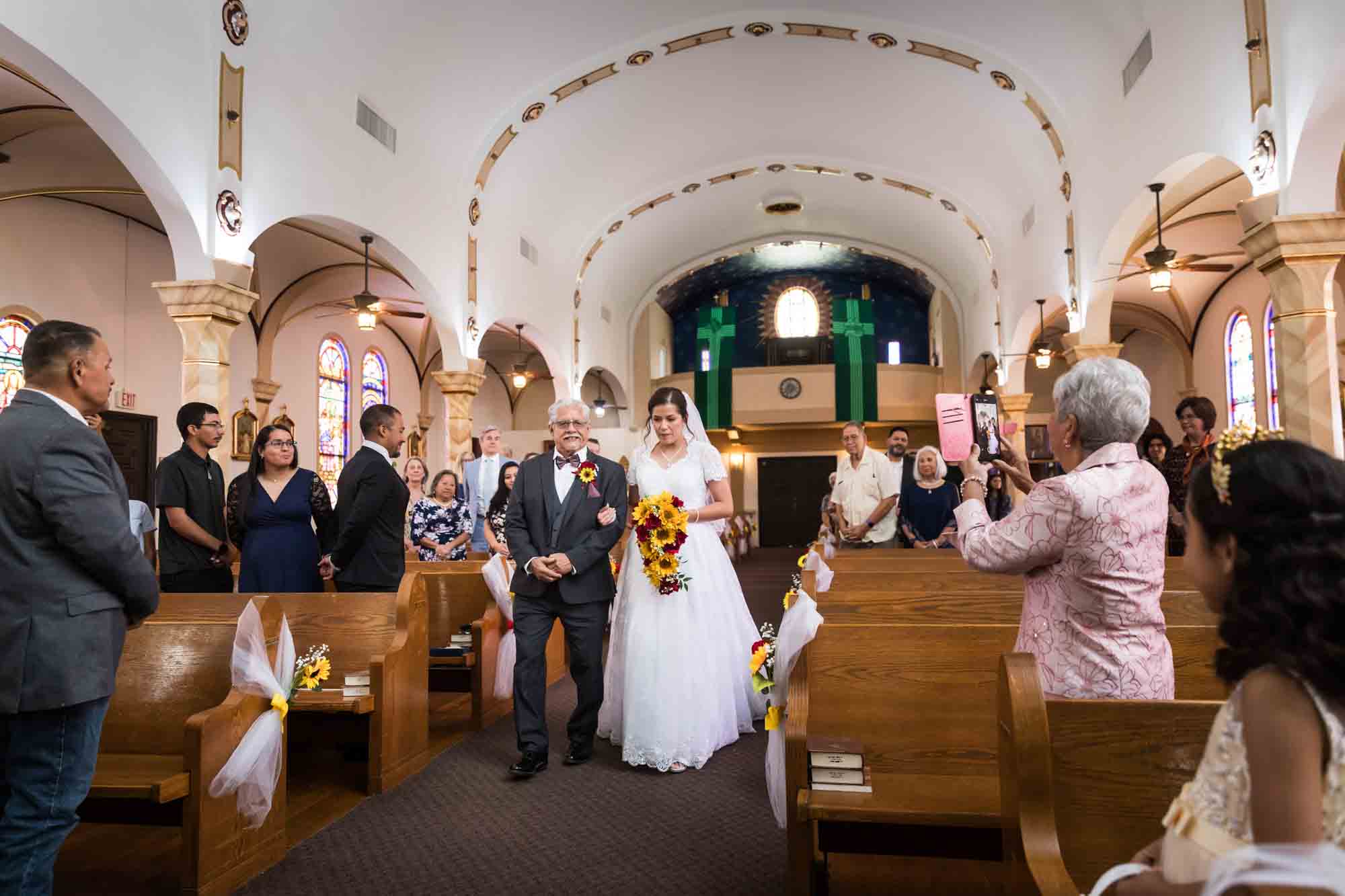 Bride and father walking down aisle in front of guests during St. Henry Catholic Church wedding