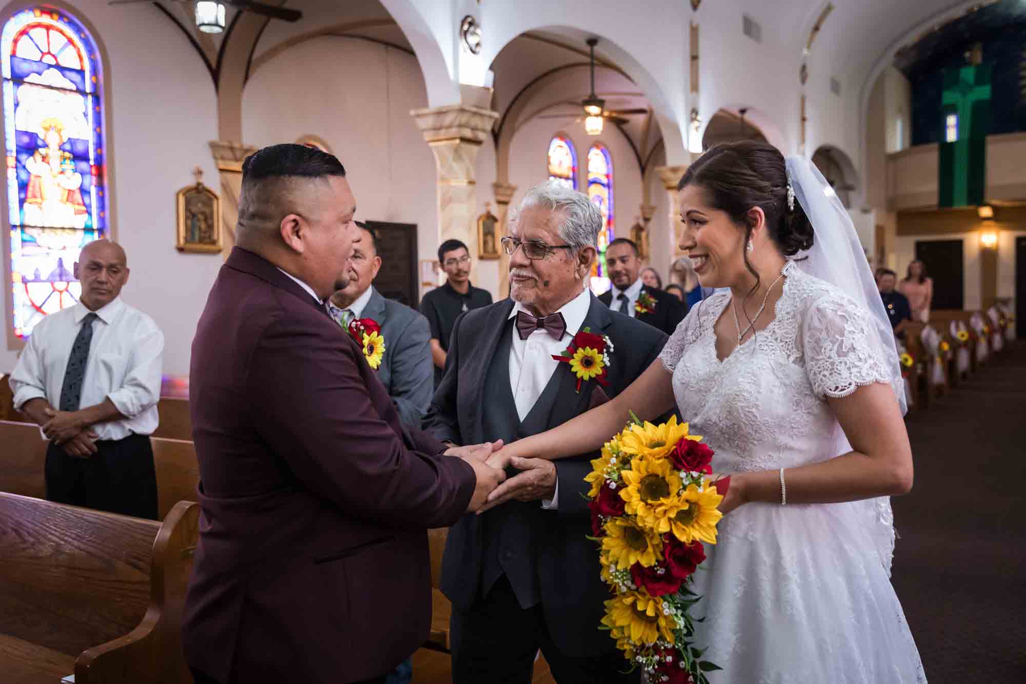 Groom accepting bride's hand in marriage from father during St. Henry Catholic Church wedding