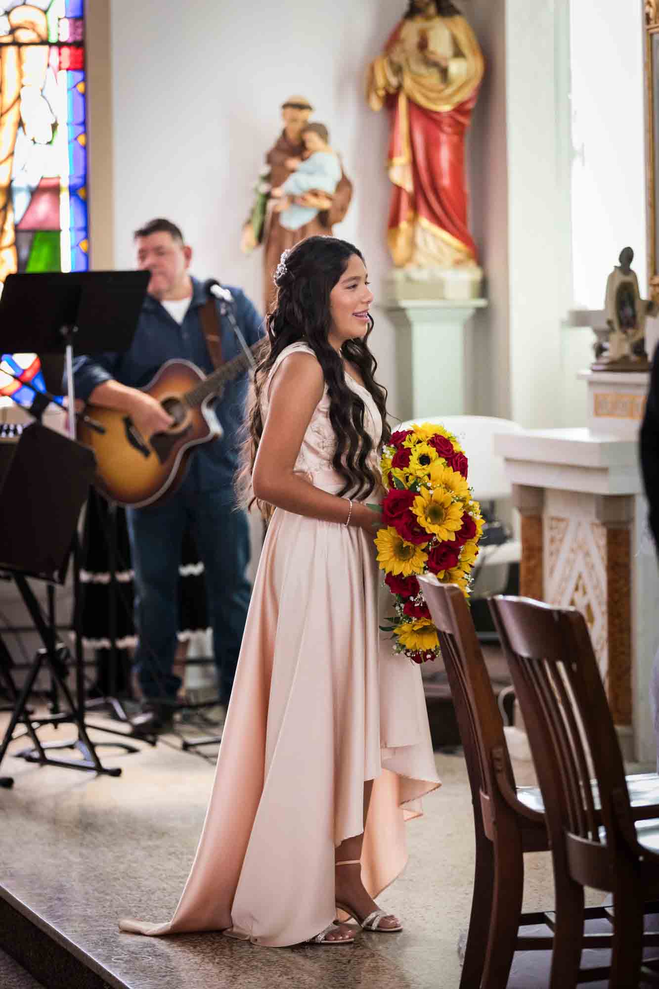 Bridesmaid wearing light pink dress holding bouquet of sunflowers and red roses