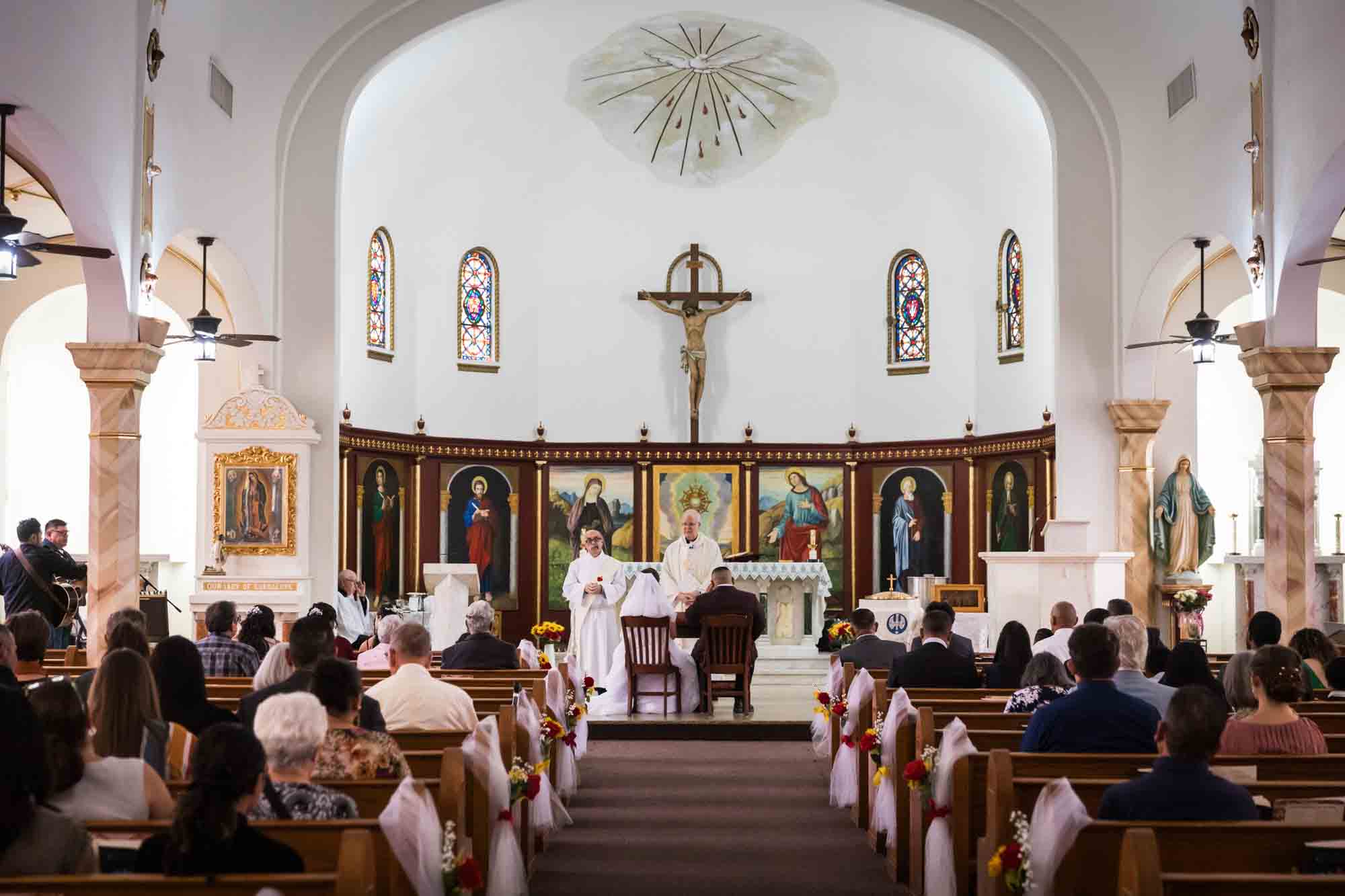 Wide shot of bride and groom sitting in front of altar and guests during ceremony