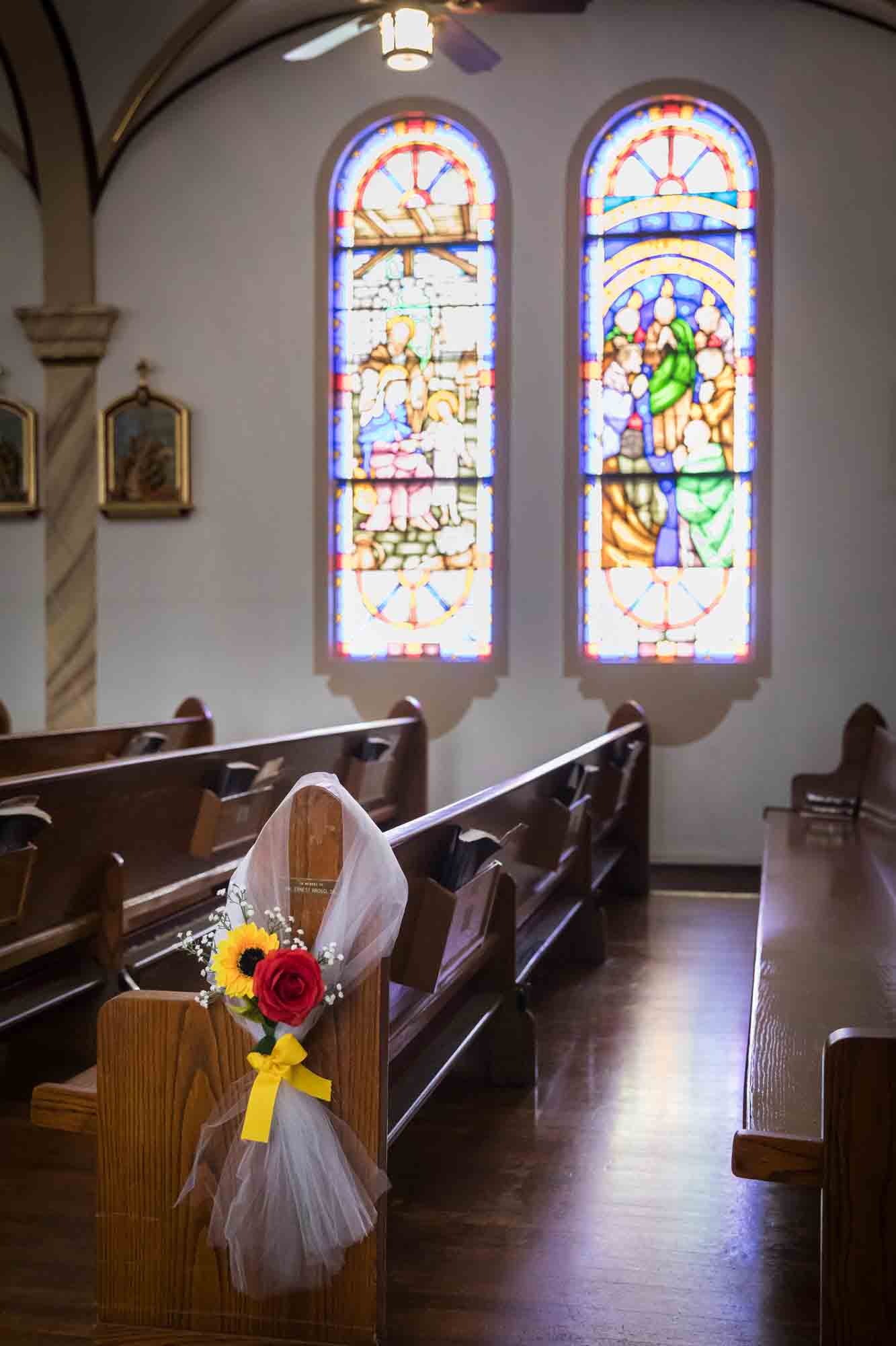 Close up of pew decorated with white tulle and flowers in front of stained glass windows