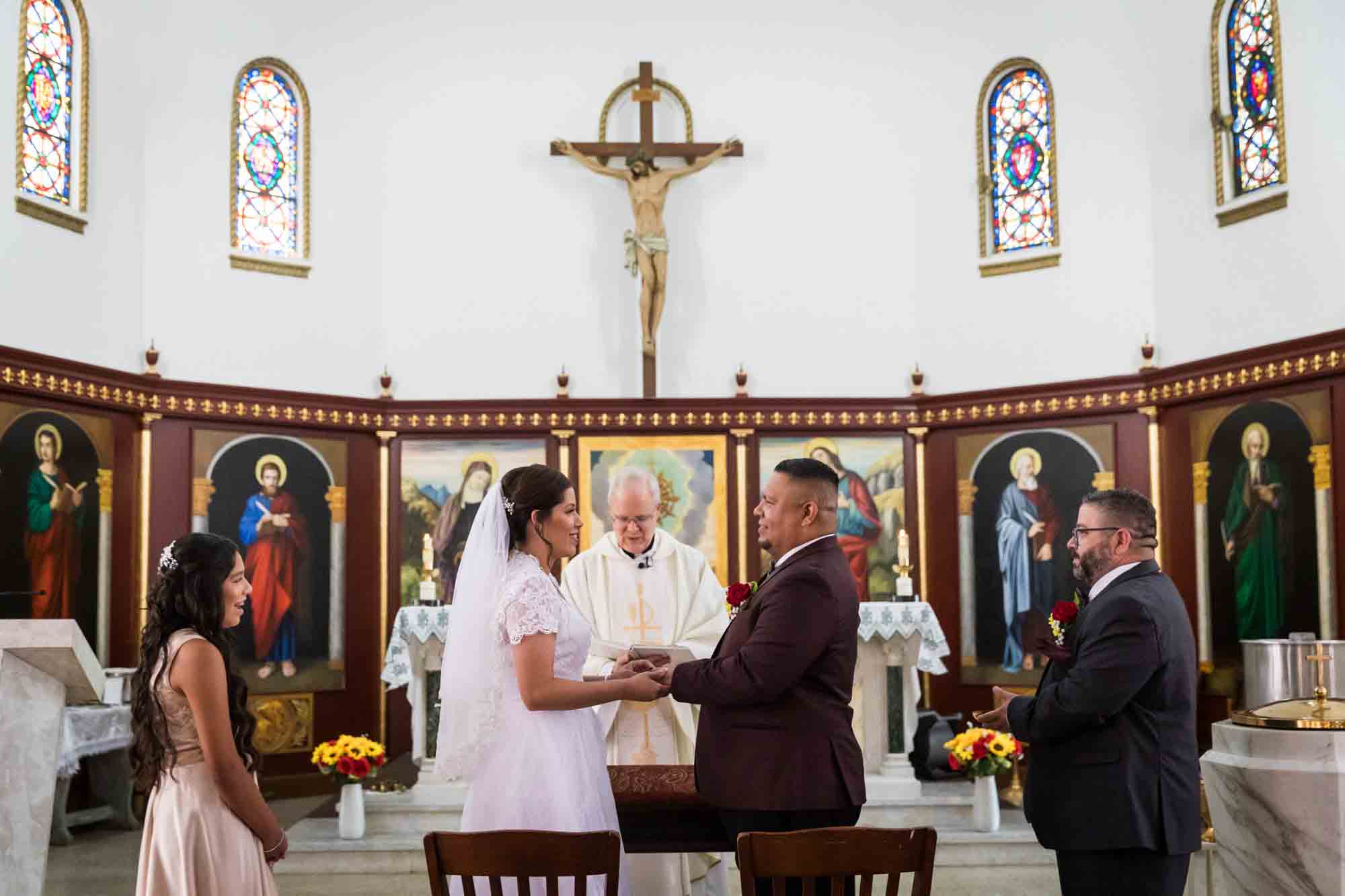 St. Henry Catholic Church wedding photos of bride and groom holding hands in front of priest and bridal party at altar