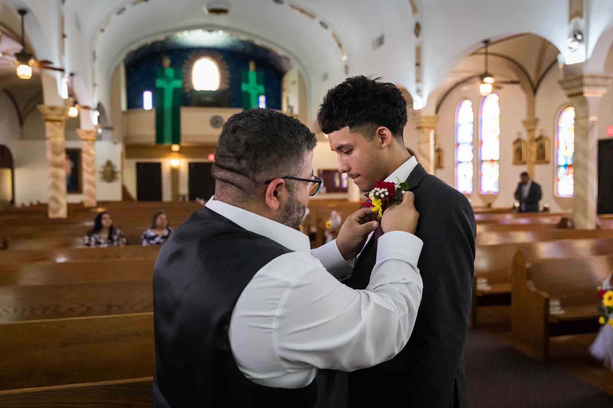 Man putting boutonniere of flowers on young man during St. Henry Catholic Church wedding