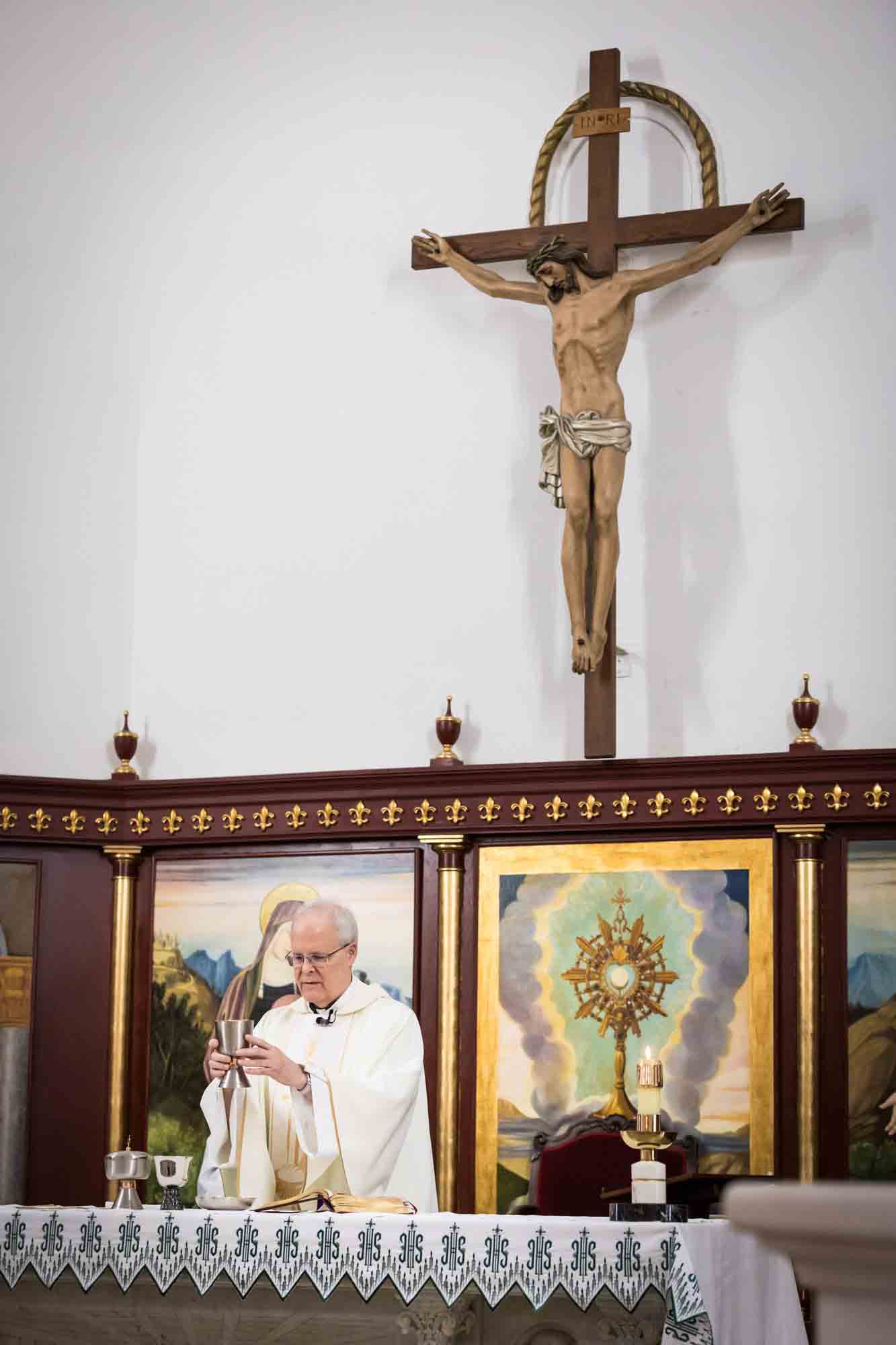 St. Henry Catholic Church wedding photos of priest holding cup in front of altar with crucifix