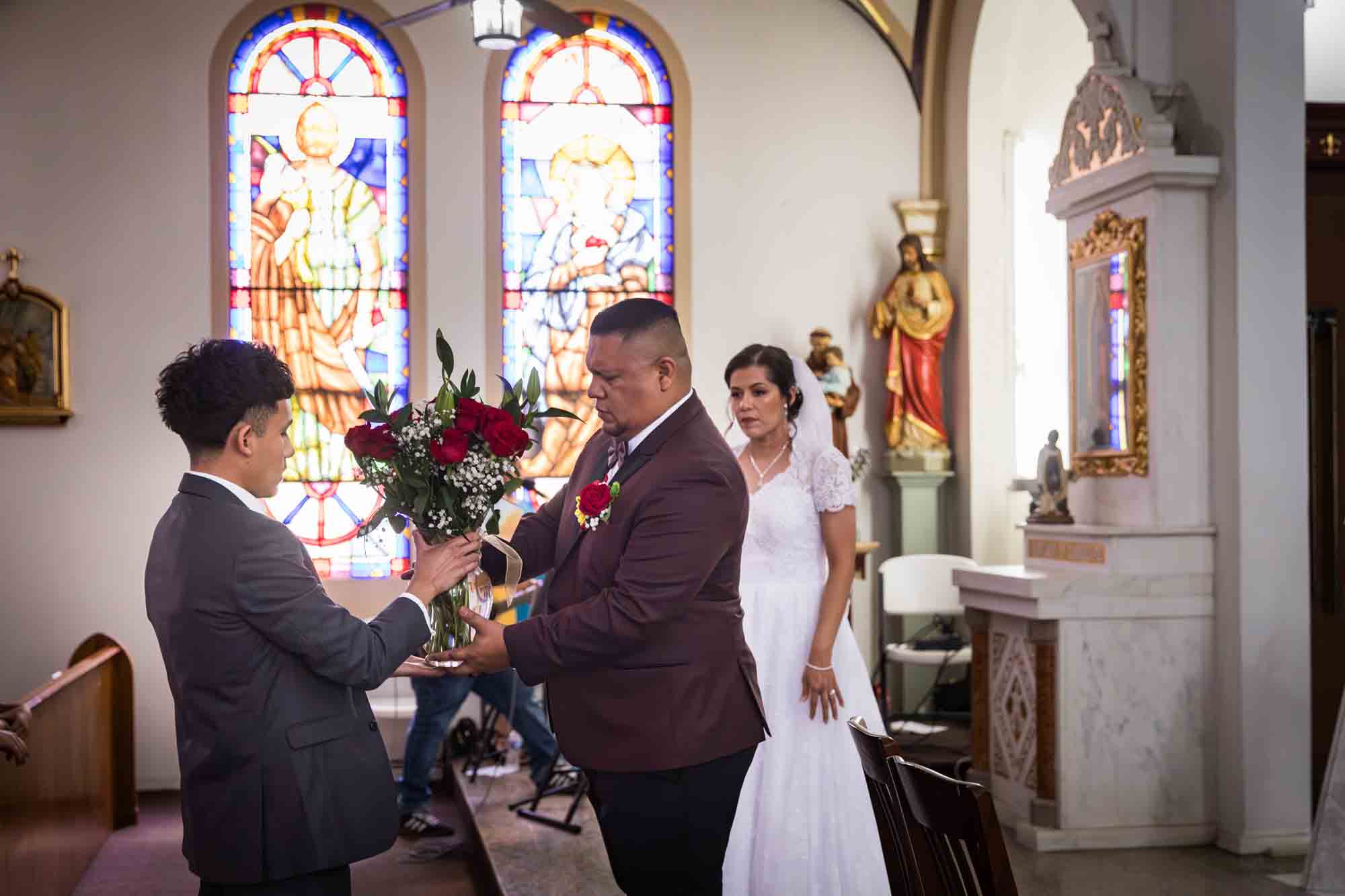 St. Henry Catholic Church wedding photos of boy giving vase or red roses to groom for the flowers to the Virgin