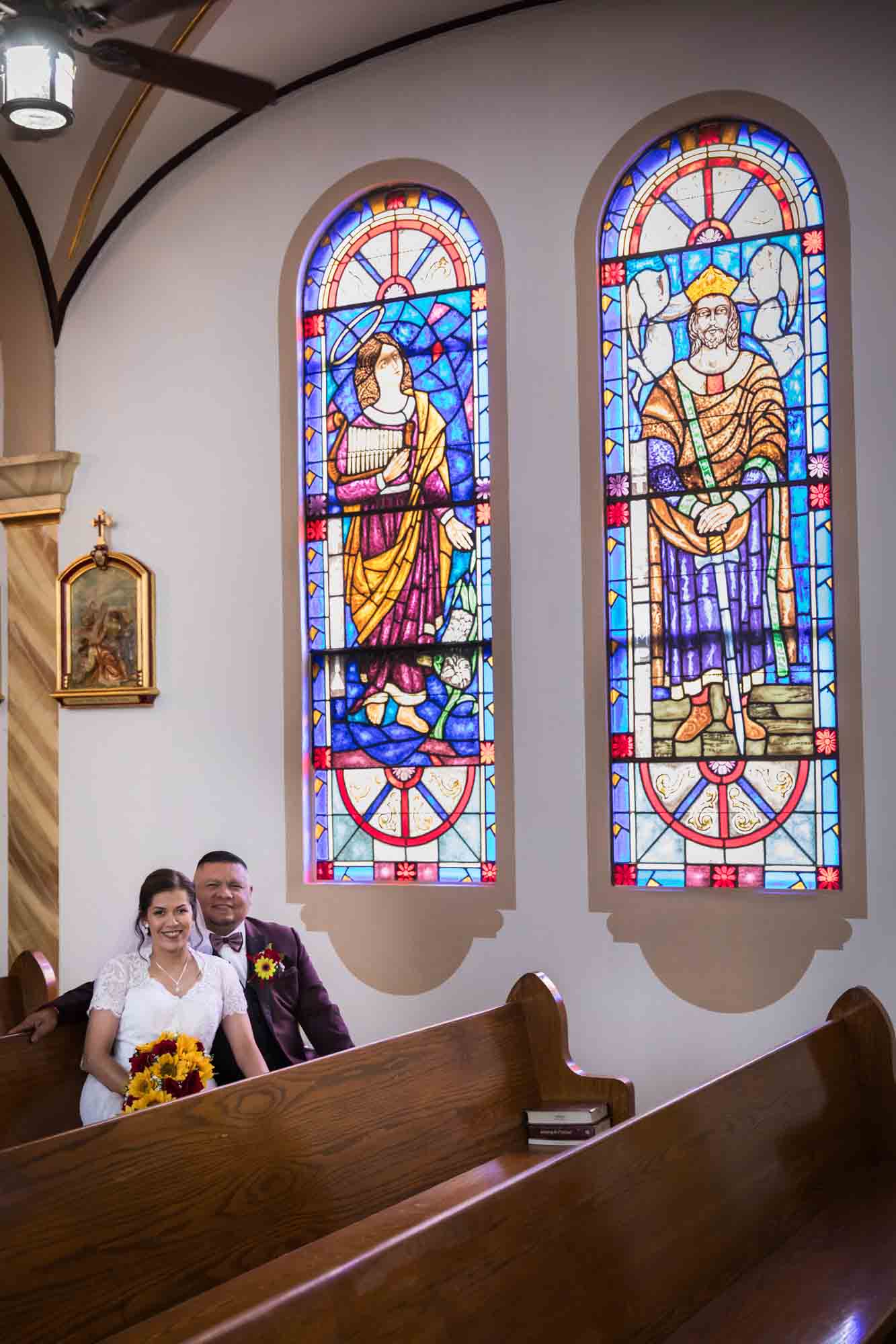 St. Henry Catholic Church wedding photos of bride and groom sitting in pew in front of stained glass window